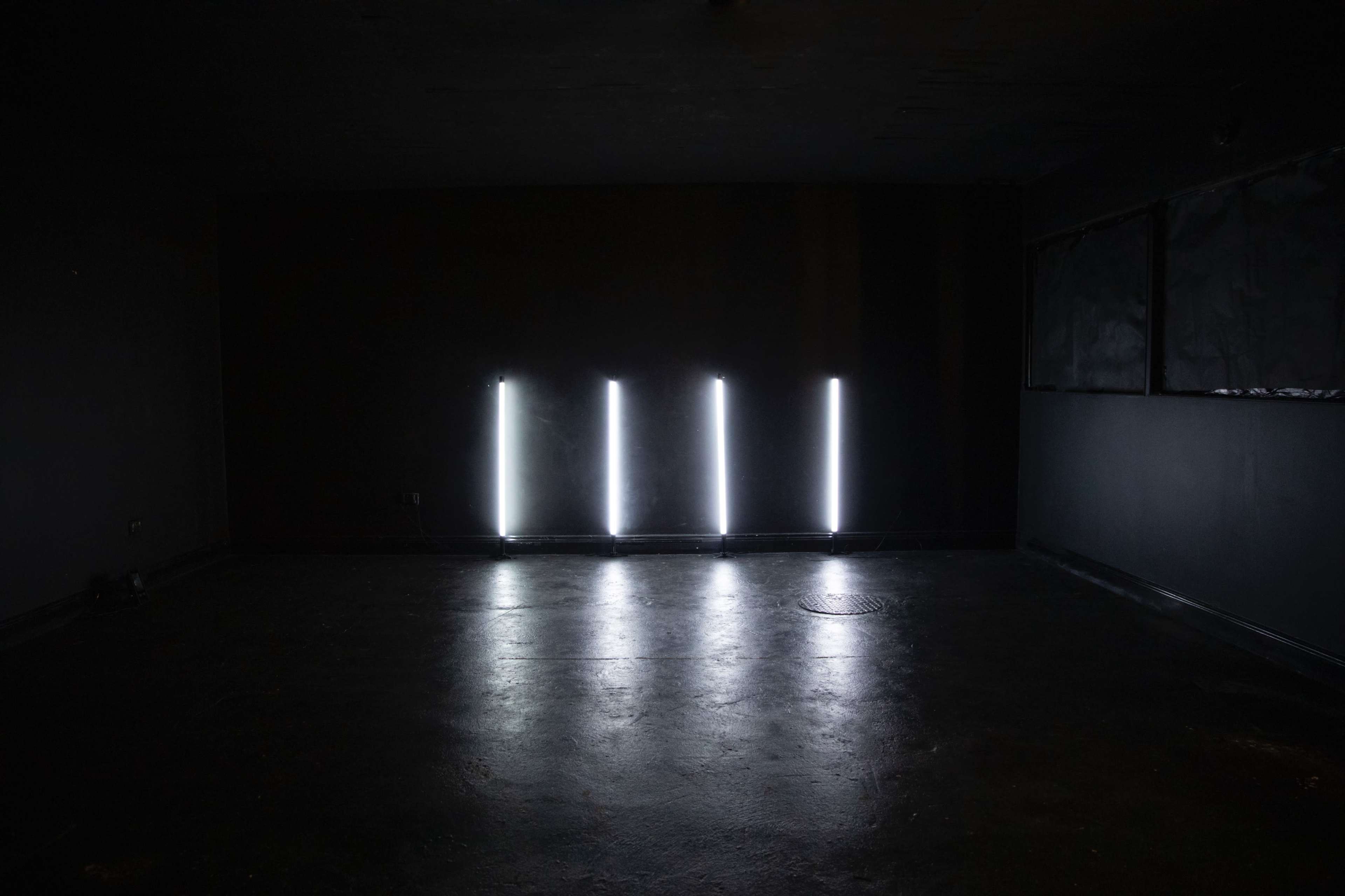 A dimly lit room with four vertical light fixtures illuminating the floor against a dark background.
