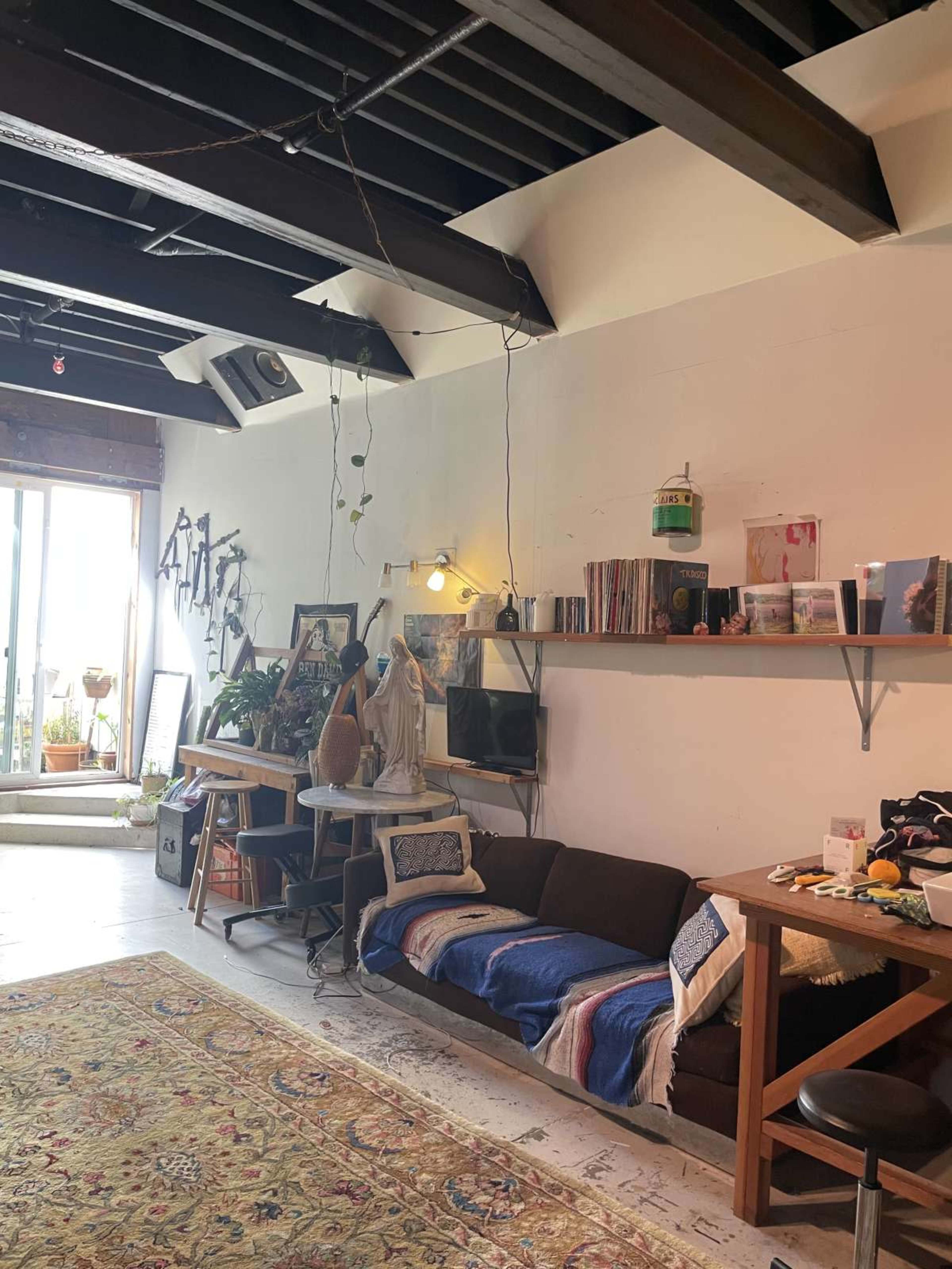The image shows an interior living space featuring a couch, a wooden table, wall art, and a large window with natural light.
