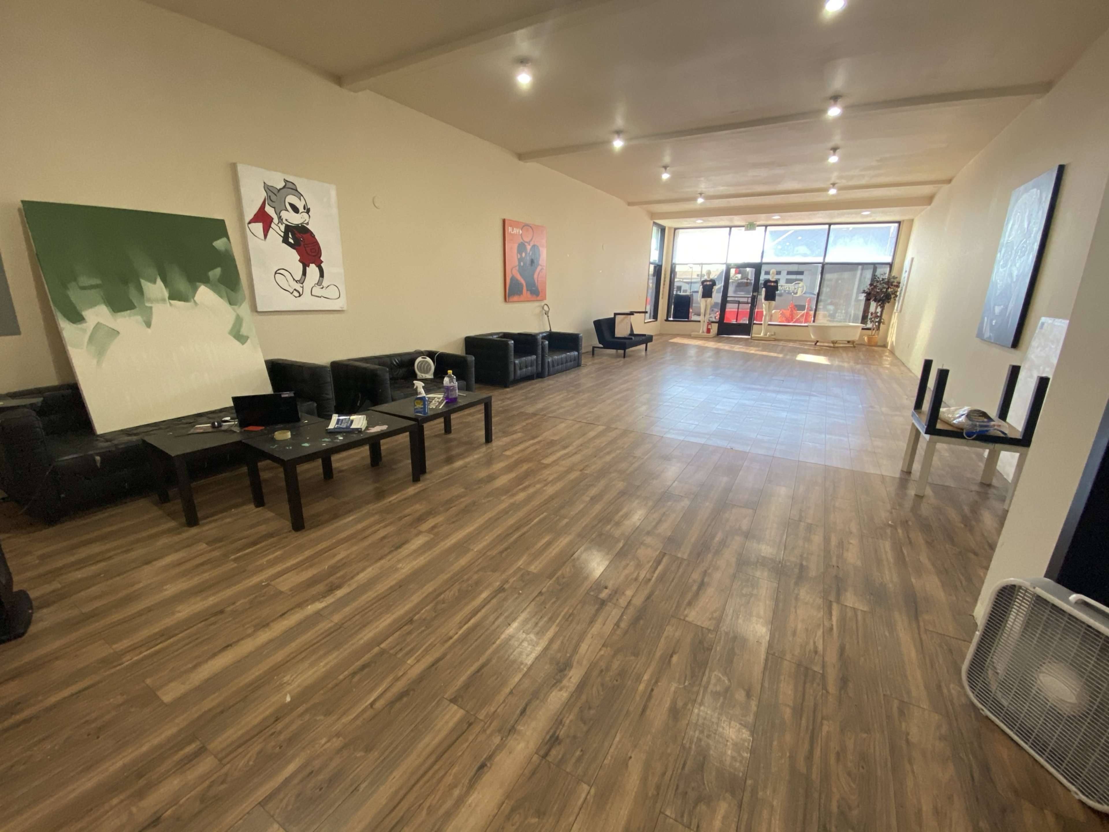 A spacious, modern indoor area with wooden flooring, black couches, and various artworks displayed on the walls.