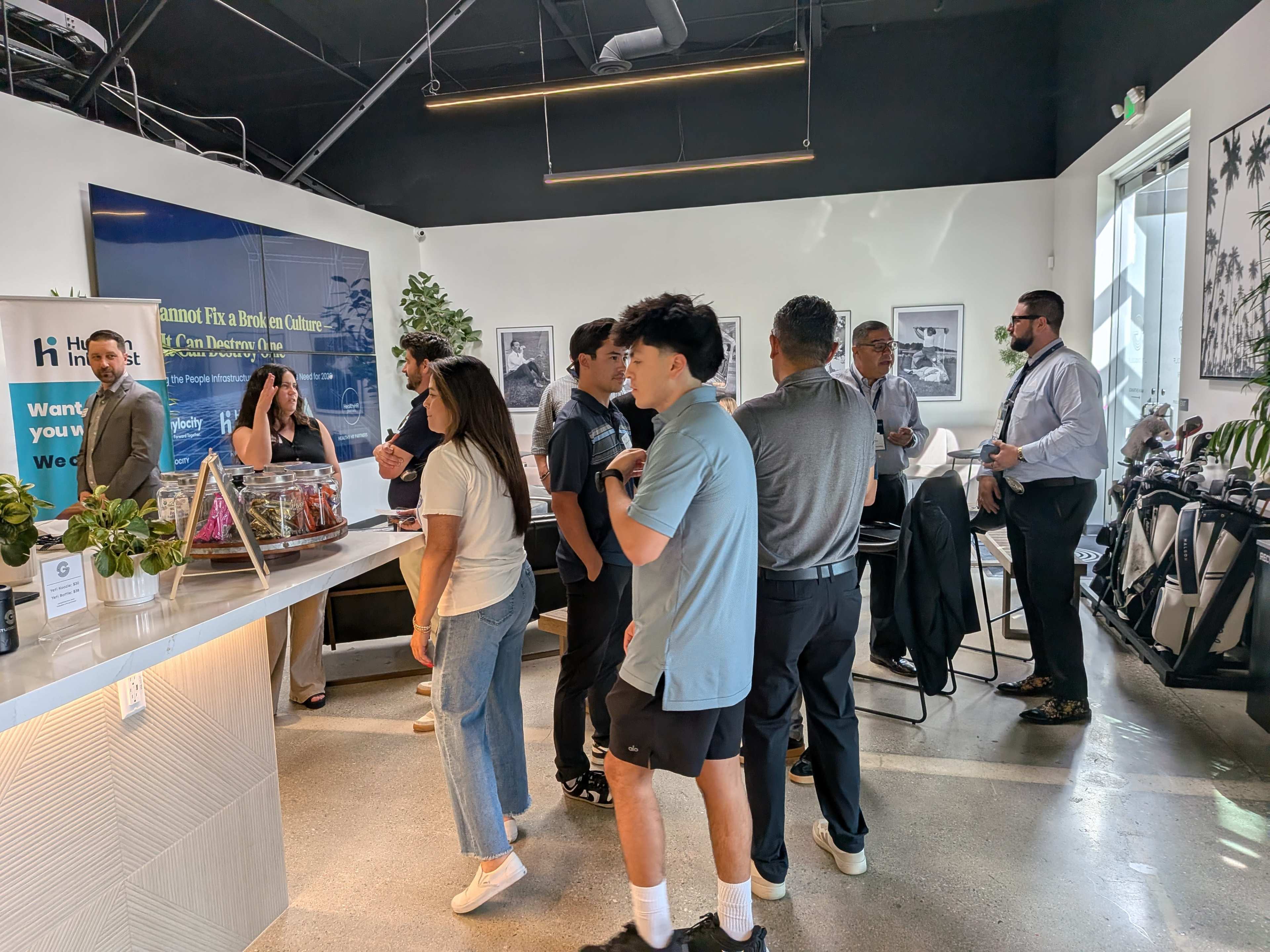 A group of people is socializing and networking inside a modern office space with large windows and a refreshment station.