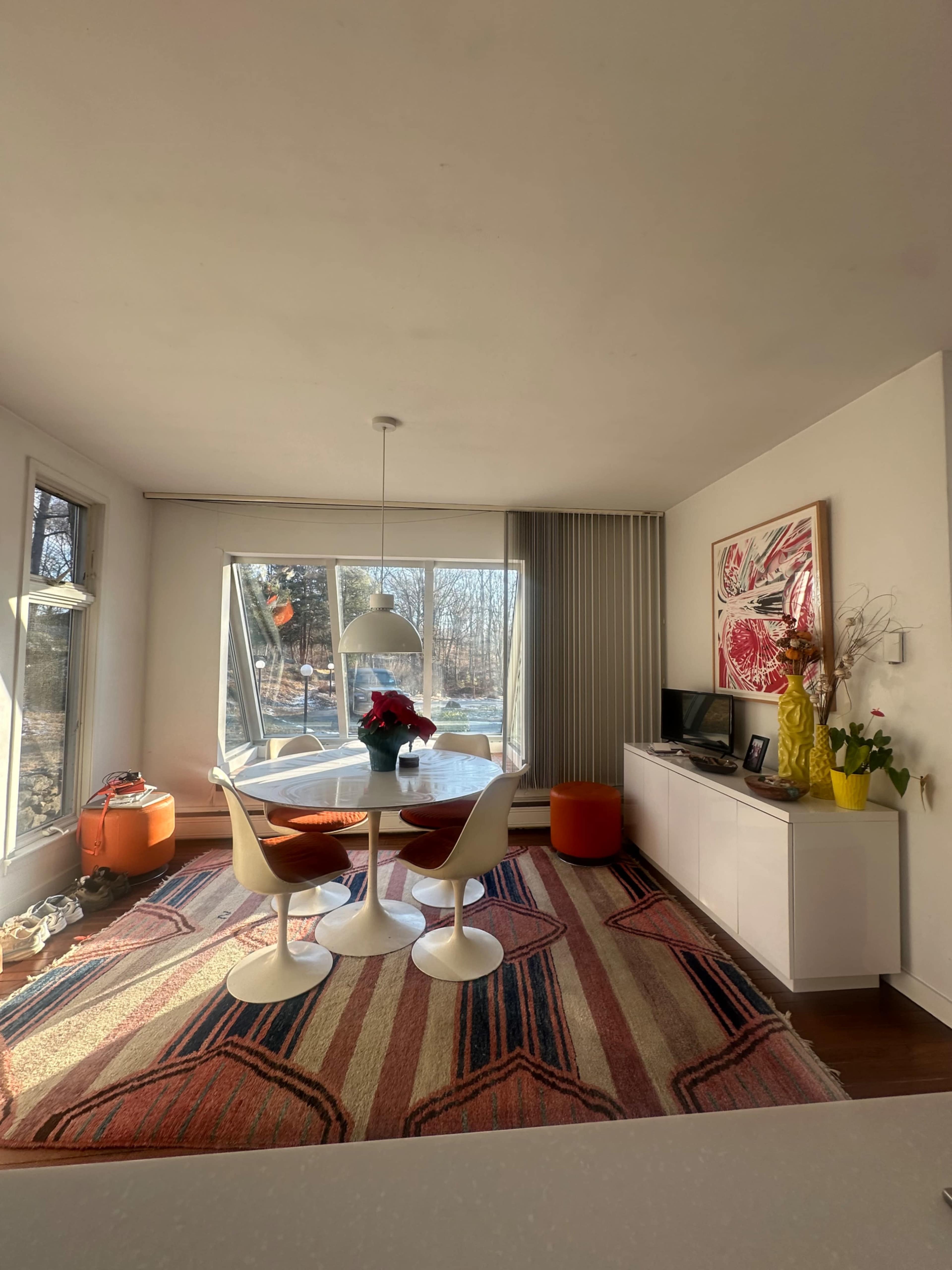 A modern dining area features a round table with four chairs, a large window with natural light, and a colorful rug.