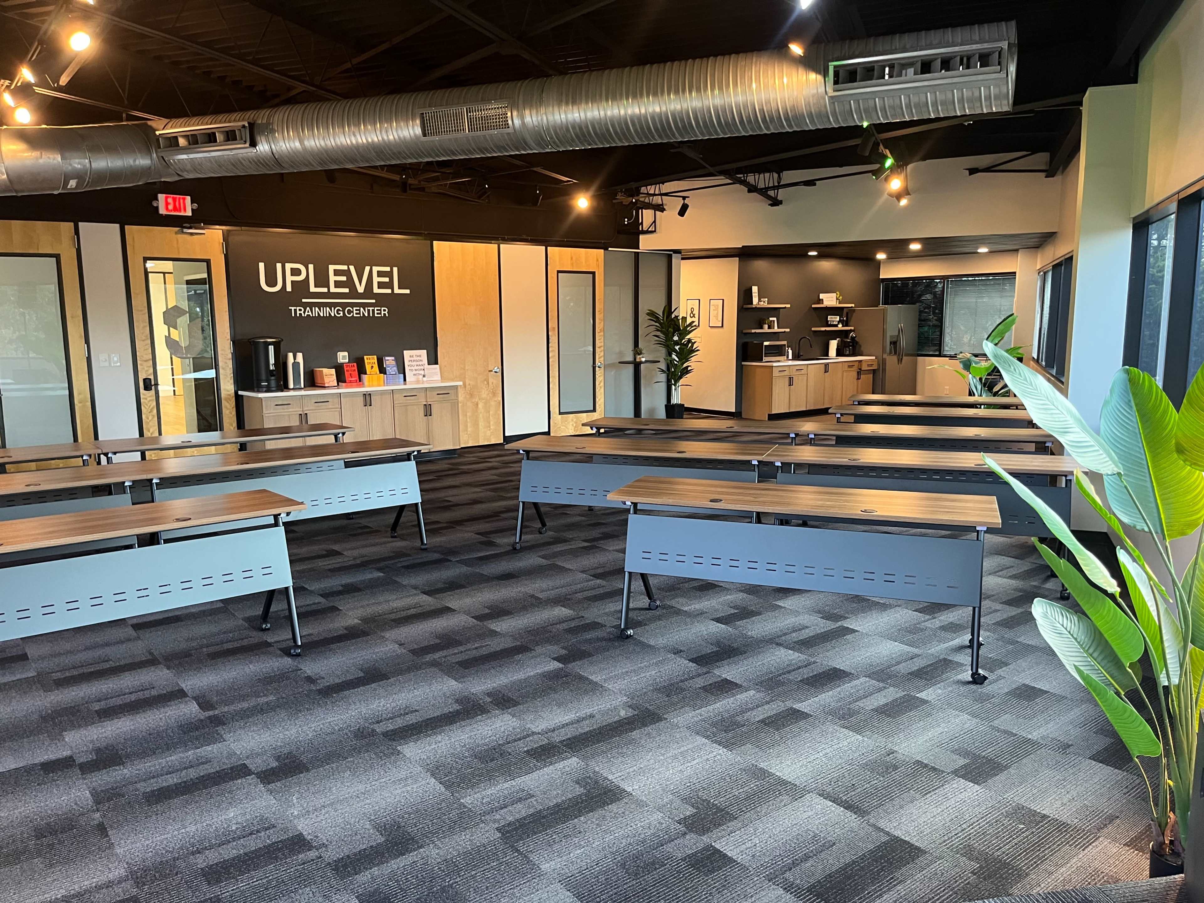 The image shows a modern training center with benches arranged in rows, a reception area in the background, and large windows allowing natural light to enter.
