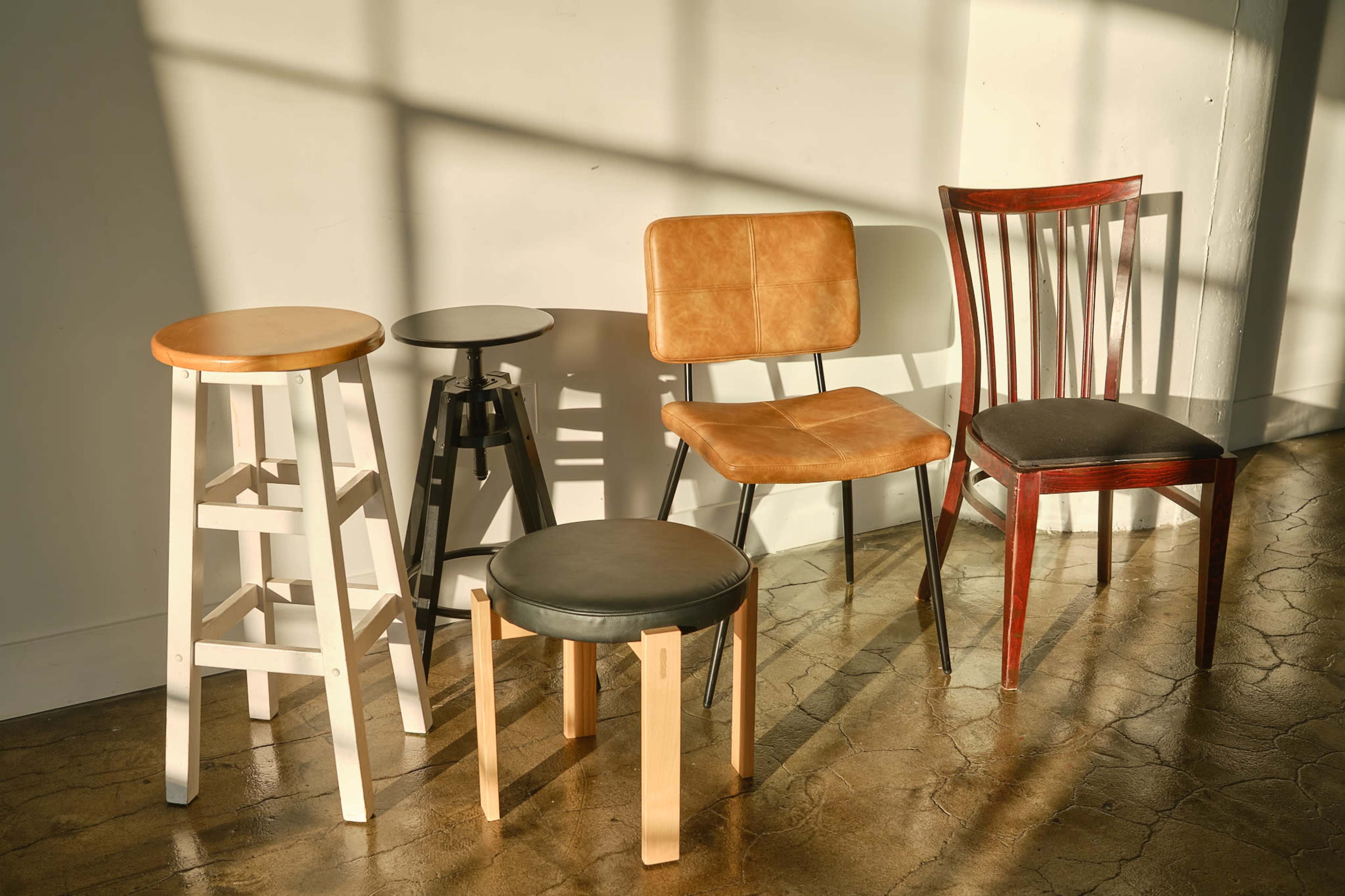 Five distinct chairs are arranged on a polished floor, with sunlight casting shadows across the wall behind them.