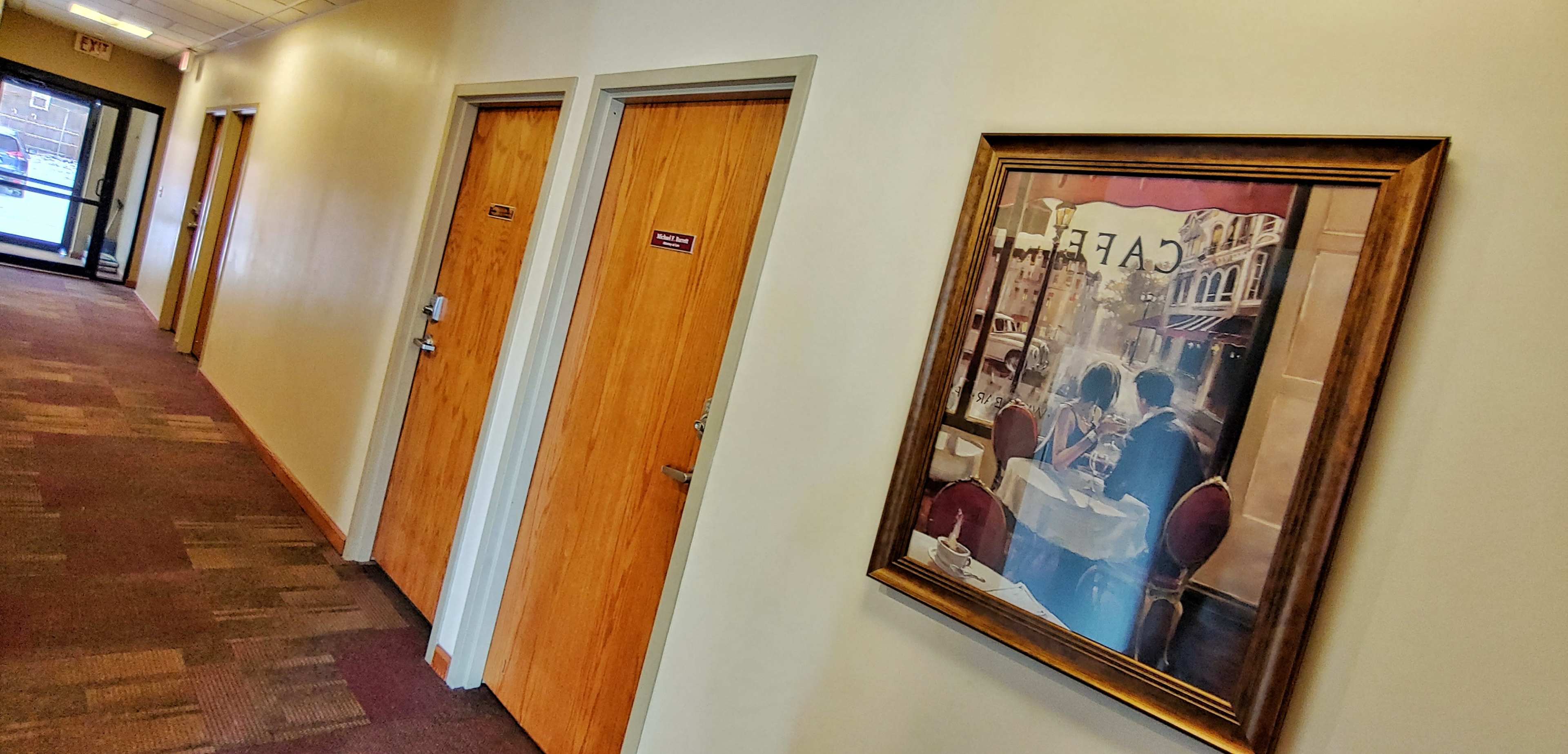 A corridor with two wooden doors on the right and a framed painting of a café scene on the left wall.