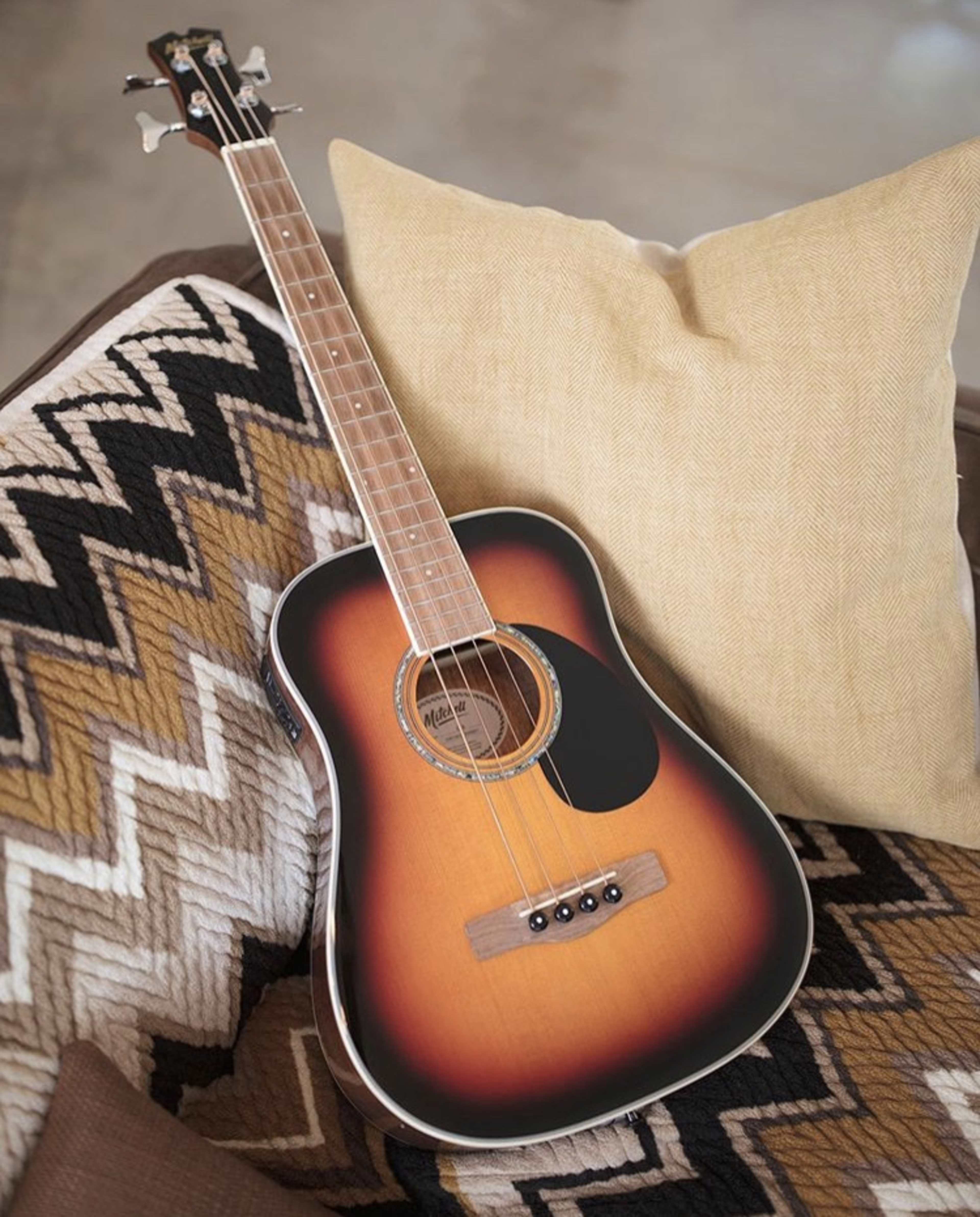 An acoustic guitar with a sunburst finish rests on a patterned couch beside a beige pillow.