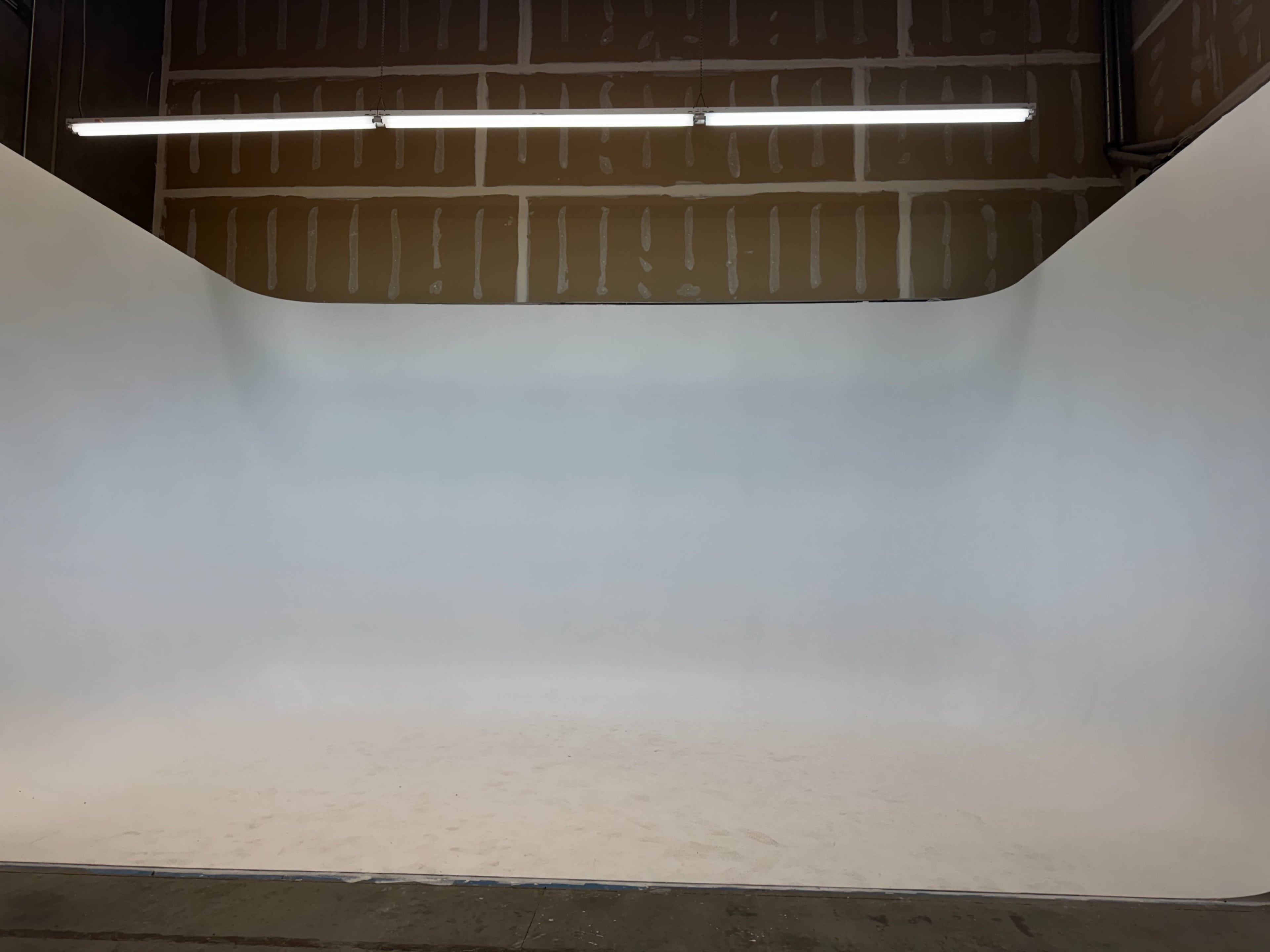 The image shows a spacious photography studio with a seamless white backdrop and exposed wooden walls.