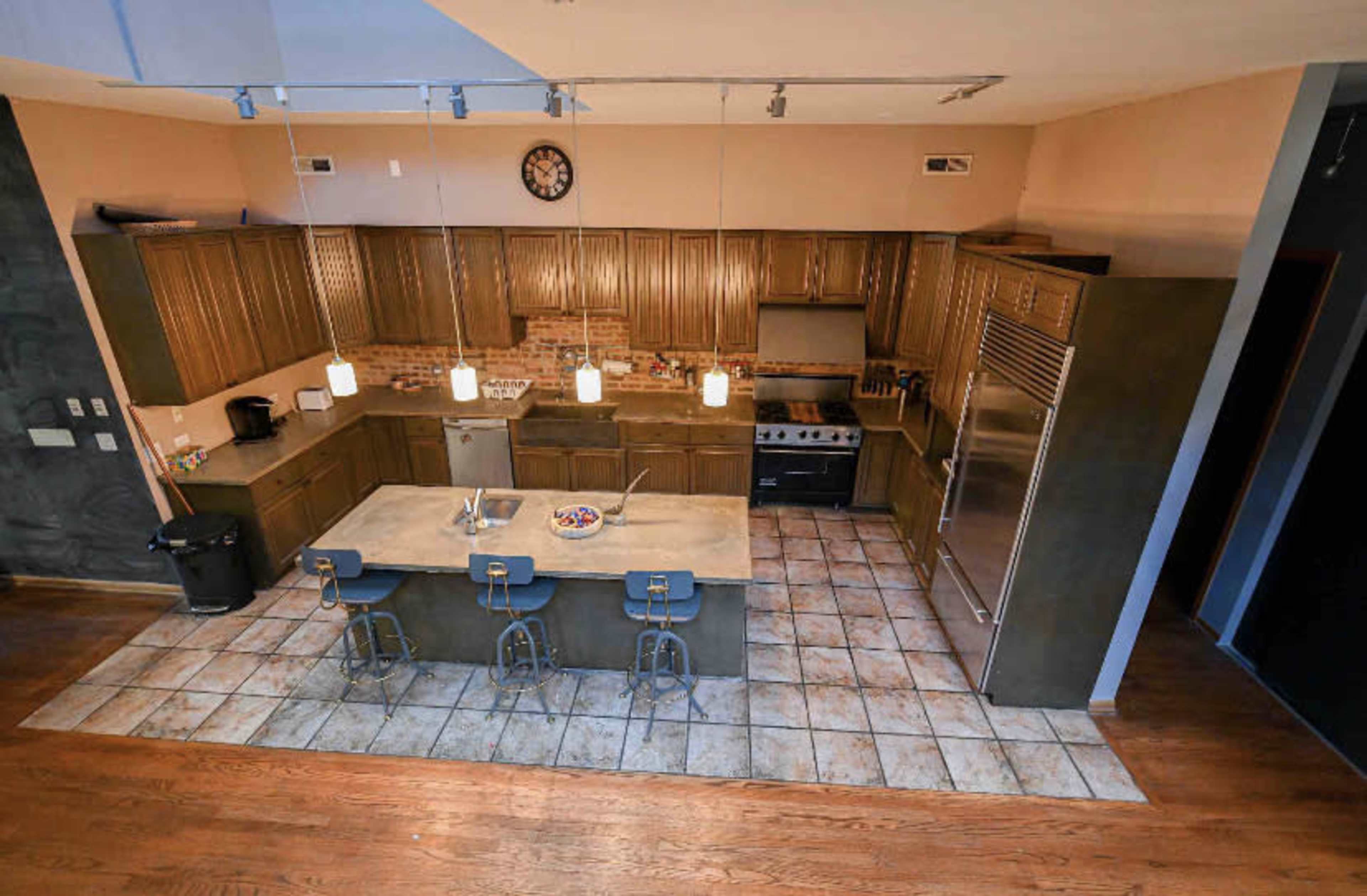 A modern kitchen with wooden cabinets, a large island with seating, and stainless steel appliances, illuminated by pendant lights.