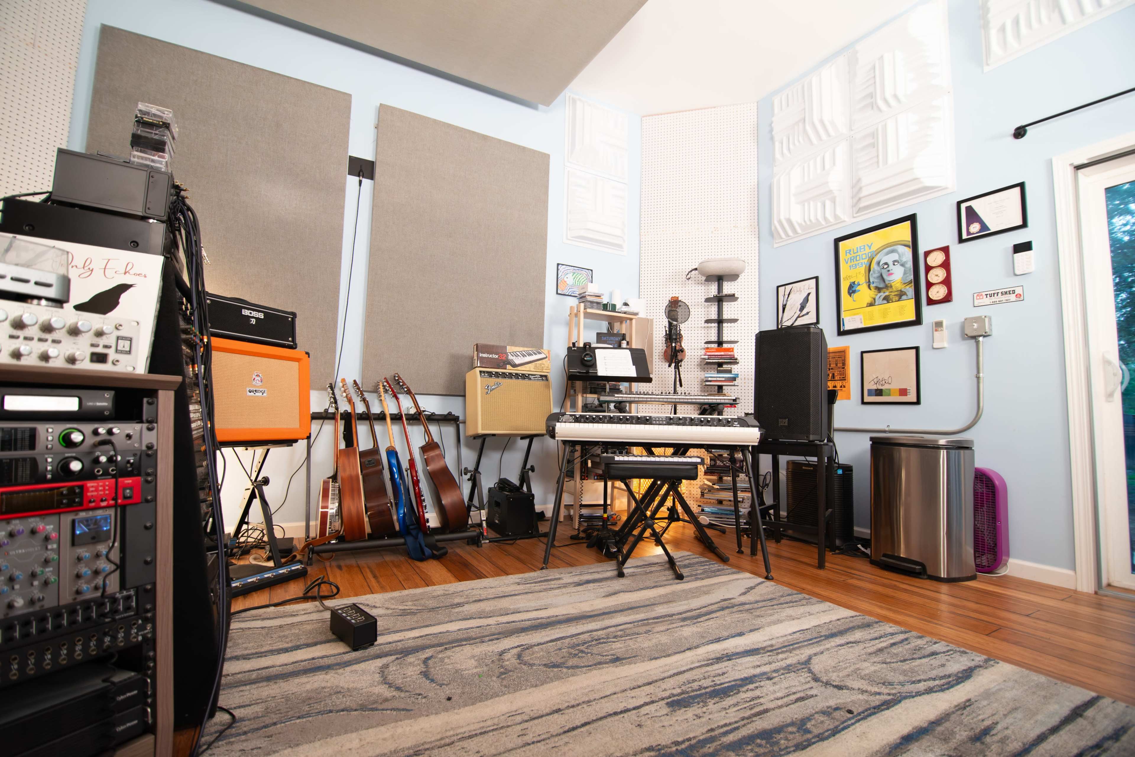 The image shows a music studio featuring various instruments, including guitars and a keyboard, along with soundproofing panels on the walls and audio equipment.
