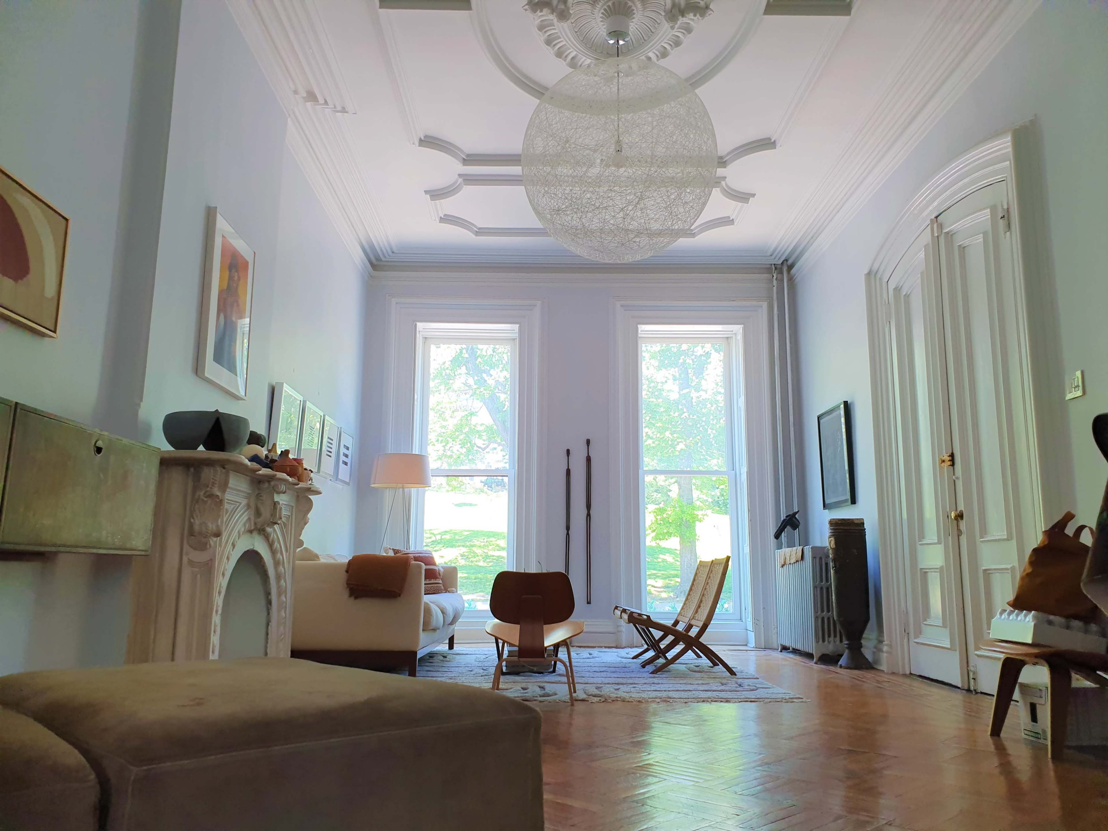 A spacious living room with large windows, a central light fixture, and a mix of modern and classic furniture.