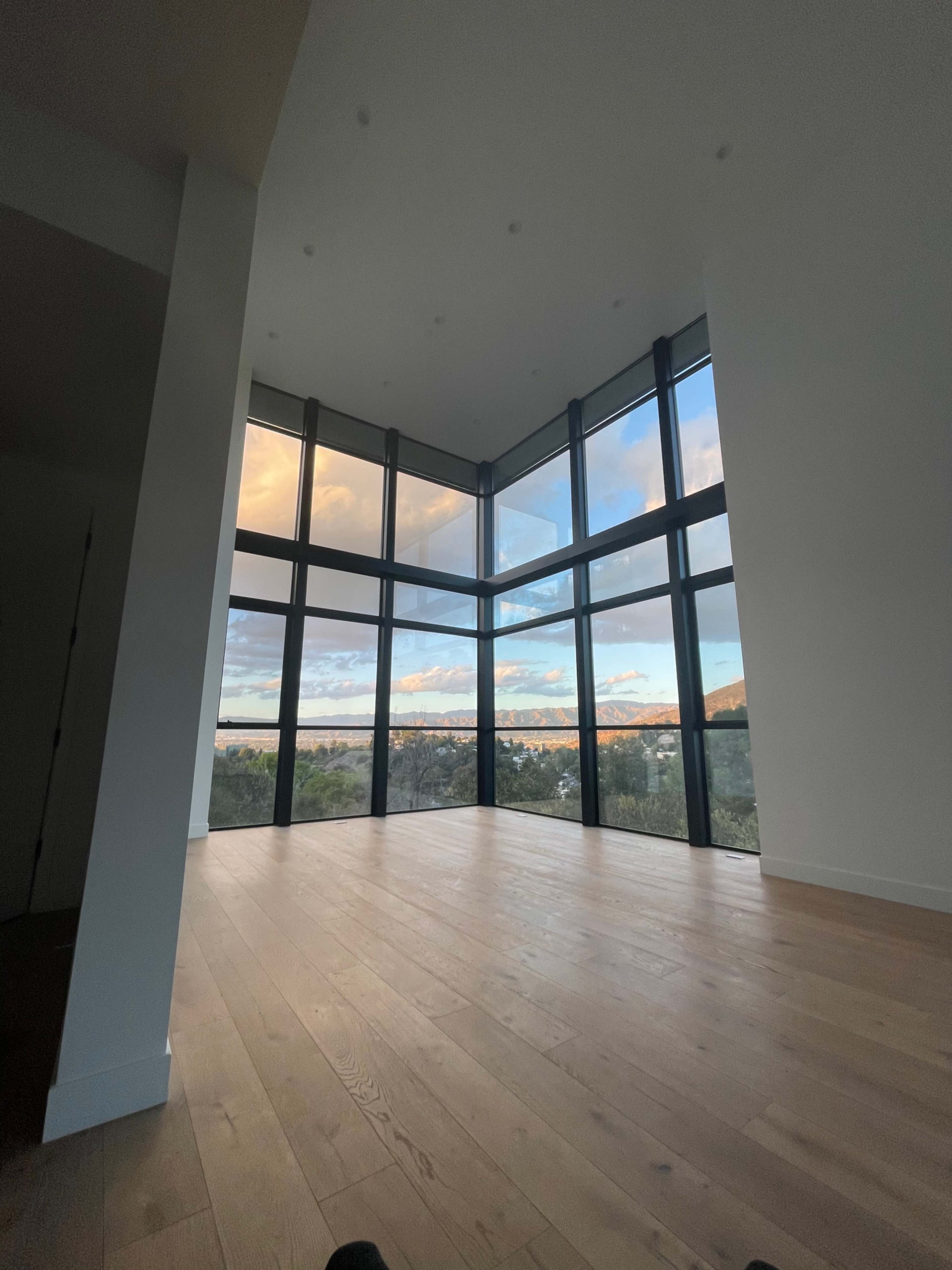 The image shows a spacious room with large windows offering a view of the landscape outside.