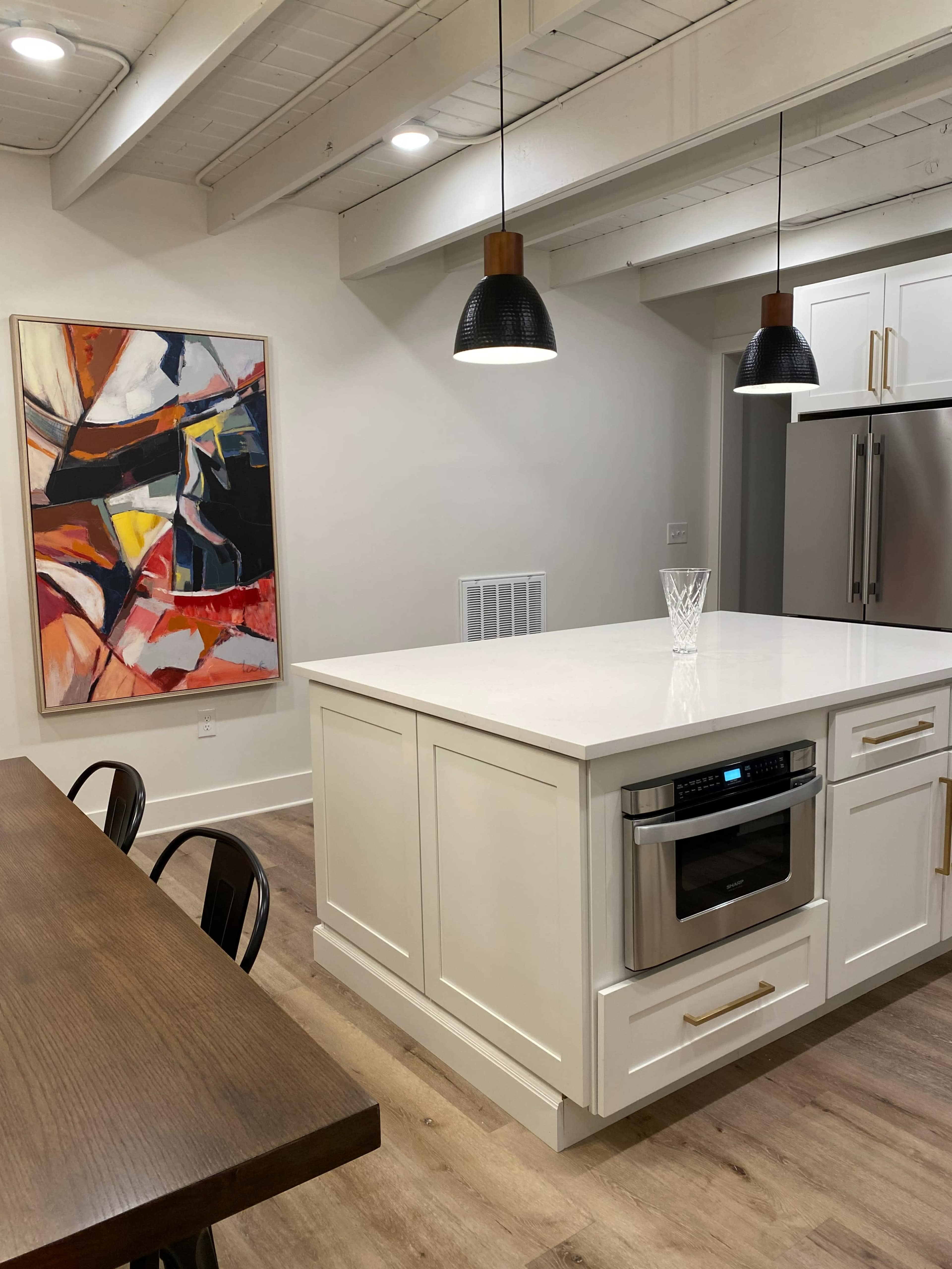 A modern kitchen featuring a large island with an oven, a dining table, and a colorful abstract painting on the wall.