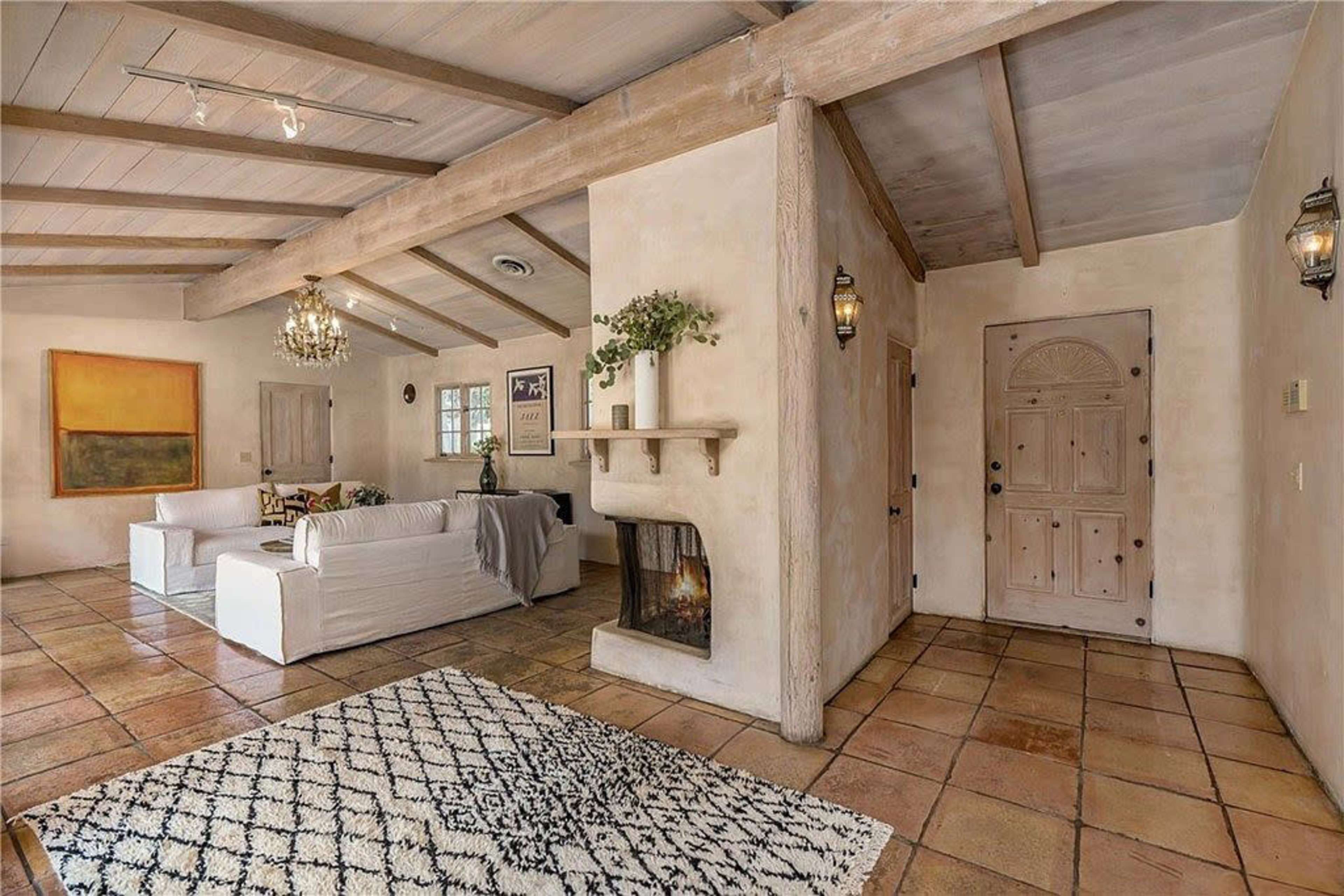 A spacious living room features a fireplace, a white sofa, and a doorway leading to an adjacent hallway.