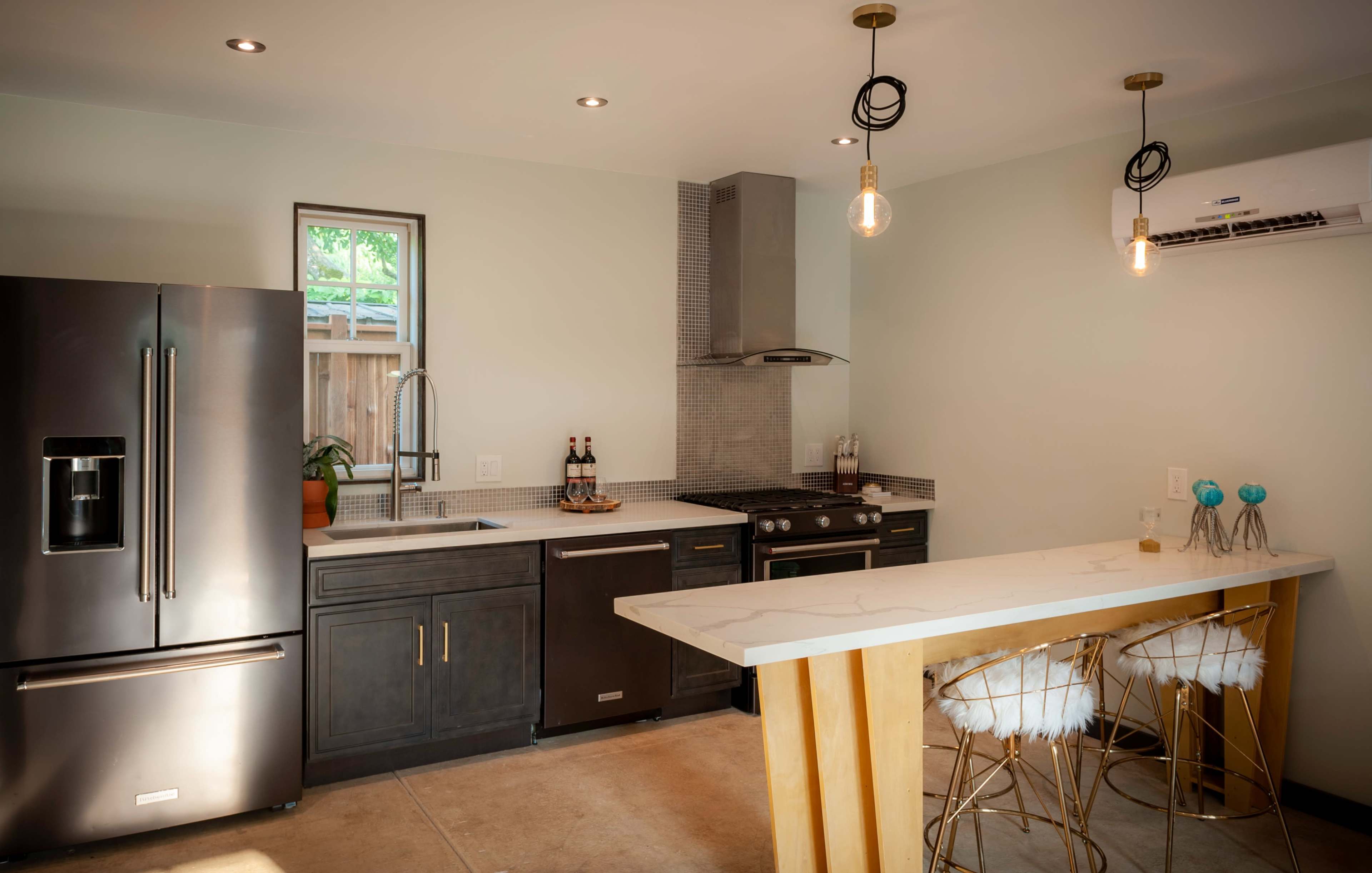 A modern kitchen with dark cabinetry, stainless steel appliances, and a countertop bar with stylish stools.