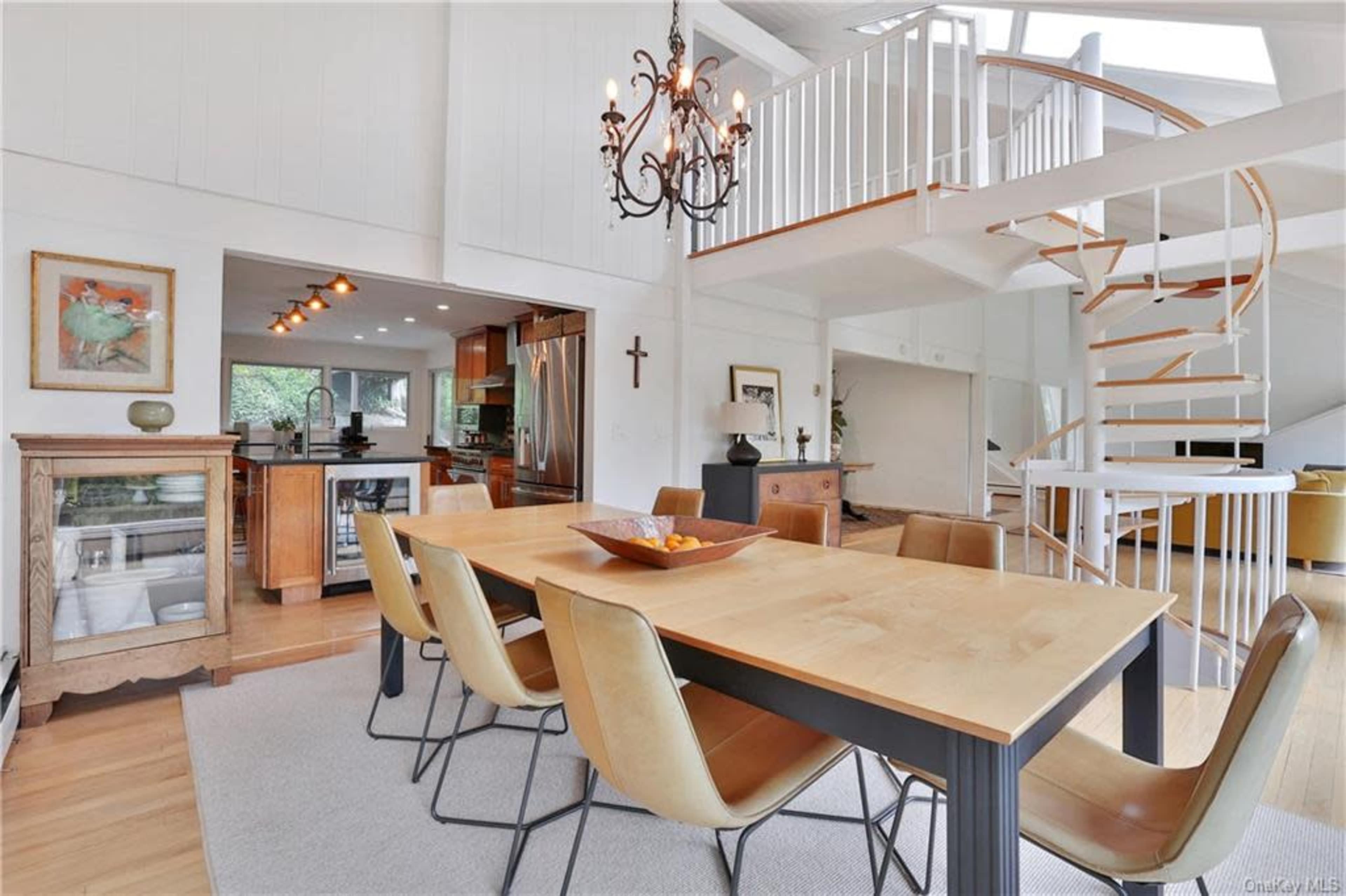 The image shows a modern dining area with a large wooden table surrounded by leather chairs, and a spiral staircase leading to an upper level.