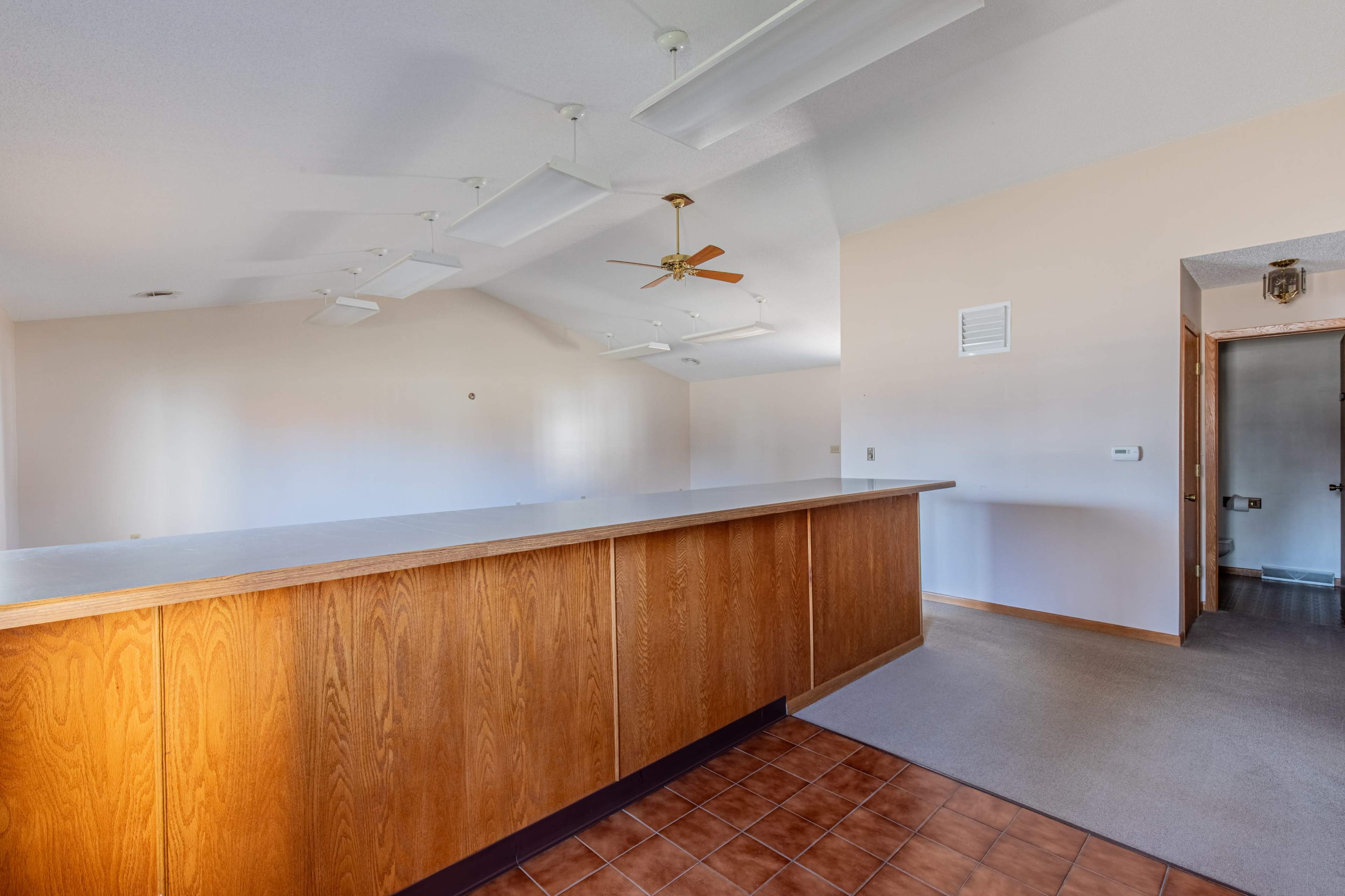 A spacious room with a wooden counter, ceiling fans, and neutral-colored walls.