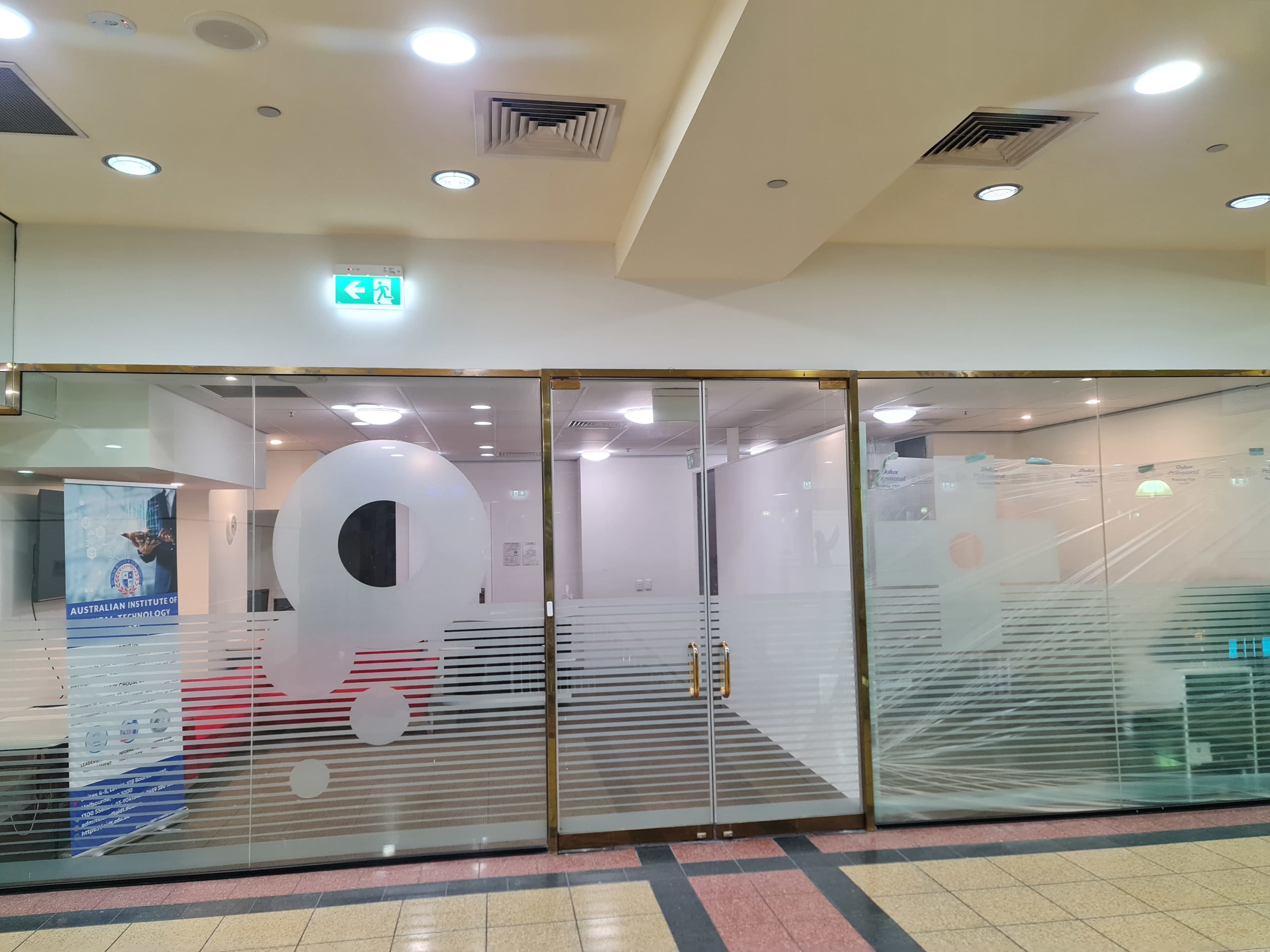 The image shows a glass office entrance with frosted designs and sliding doors, located in a commercial building.