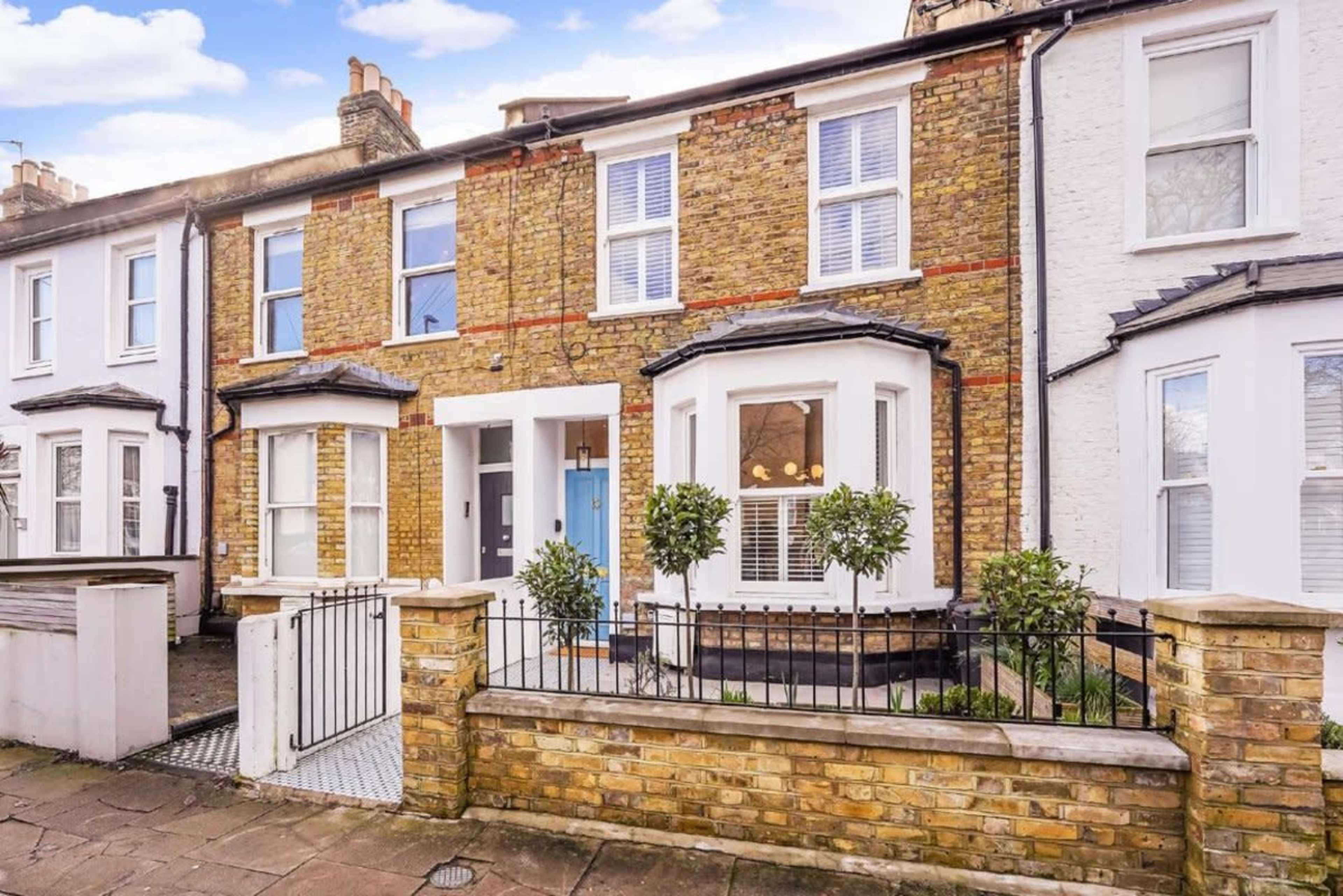 A row of attached brick houses features a blue front door and decorative plants in front of each entryway.