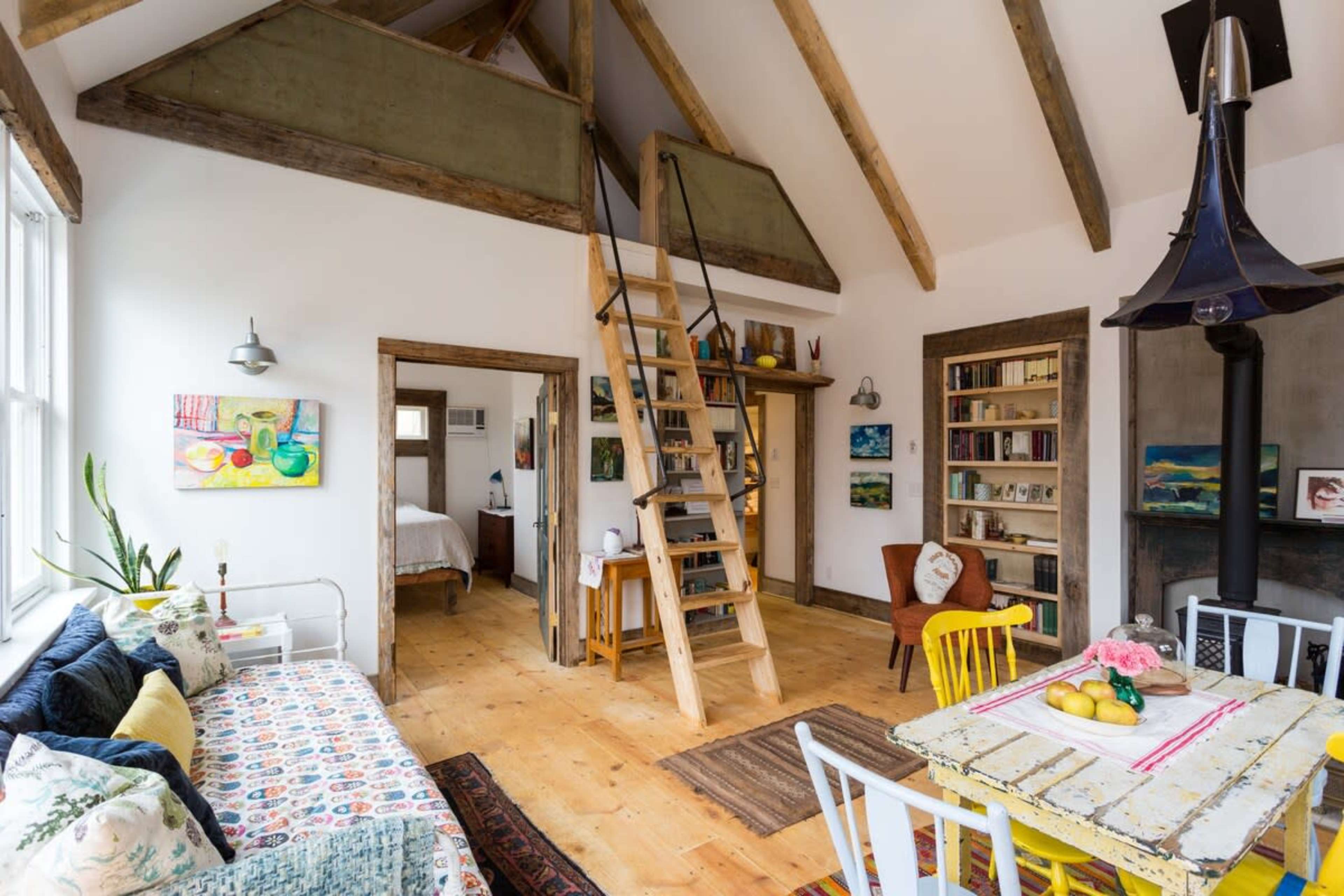 A bright, open-concept living space featuring a kitchen and dining area with a wooden table, colorful chairs, and a staircase leading to a loft.