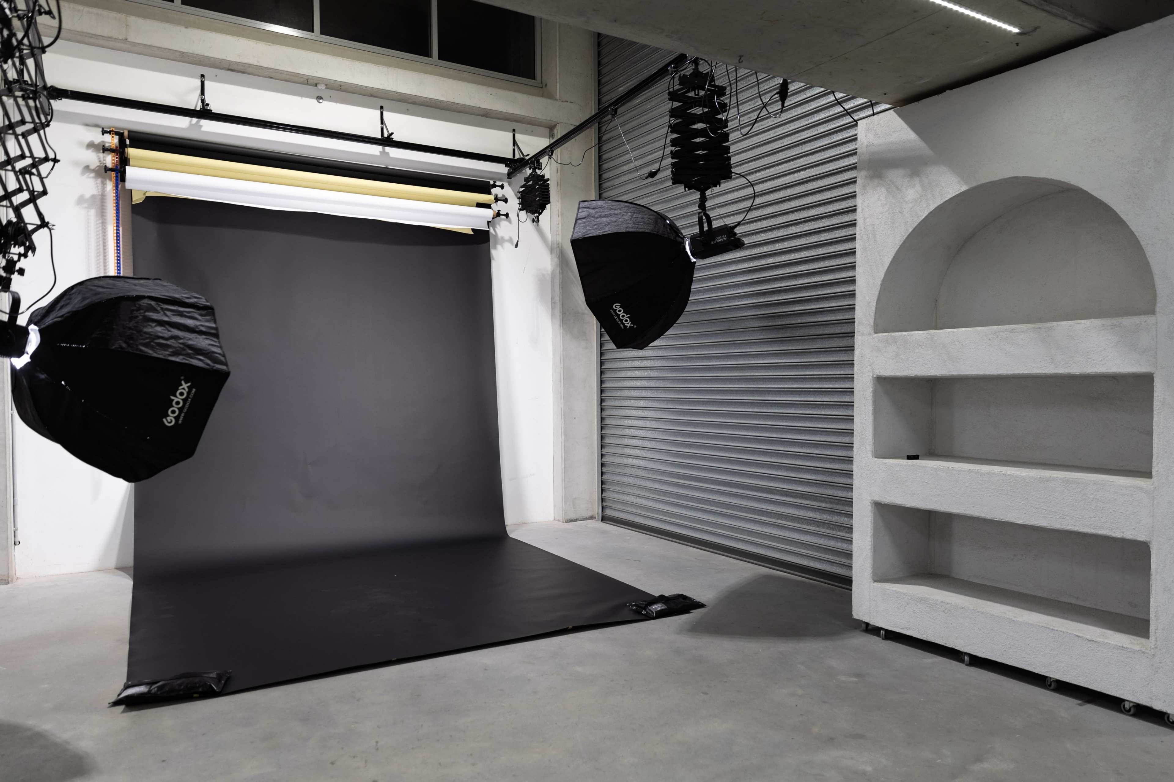 A photography studio equipped with a black backdrop, softbox lights, and a shelf against a textured wall.