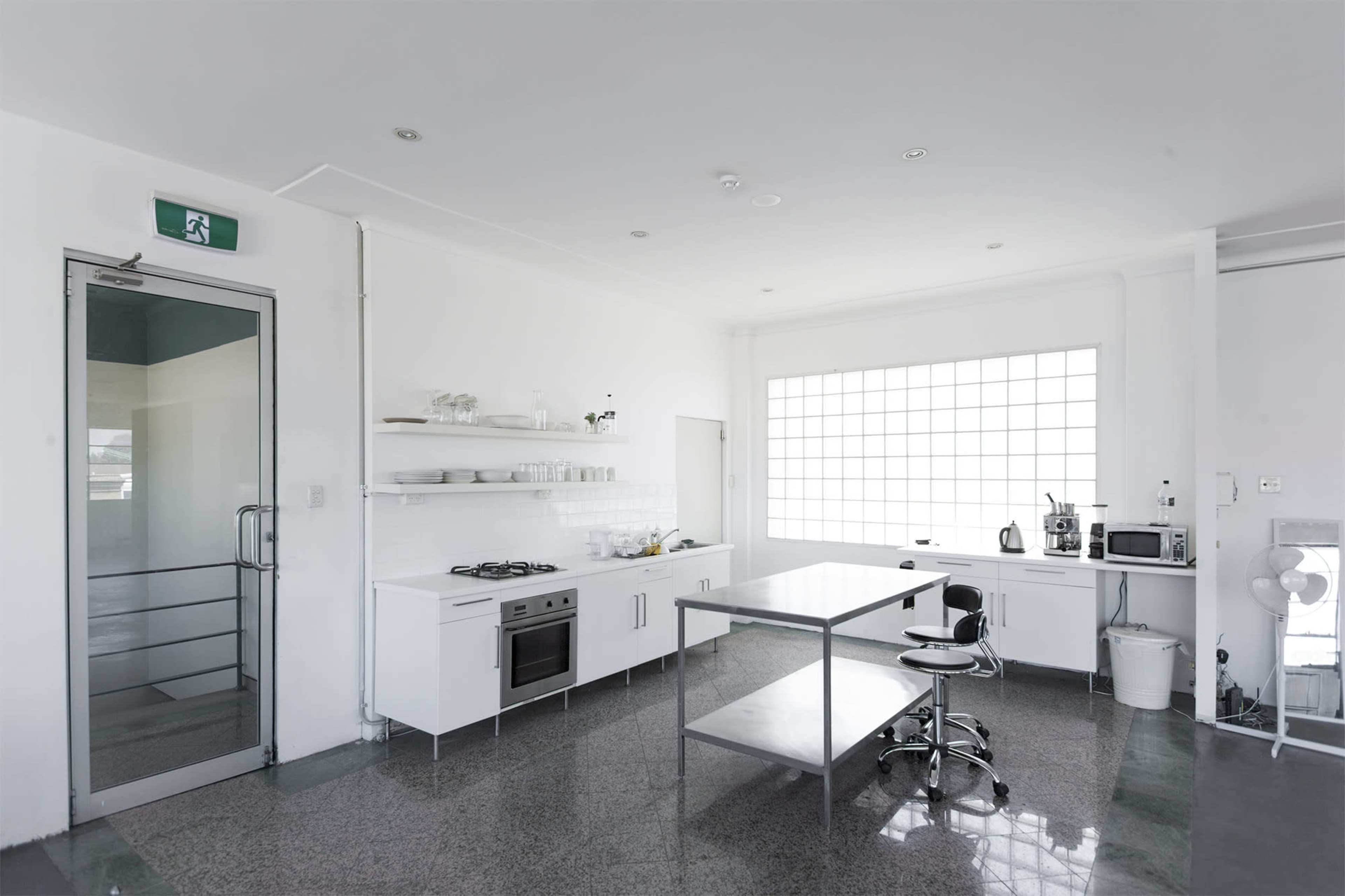 A modern kitchen features a glass door, a central table with a stool, and appliances against white cabinetry.