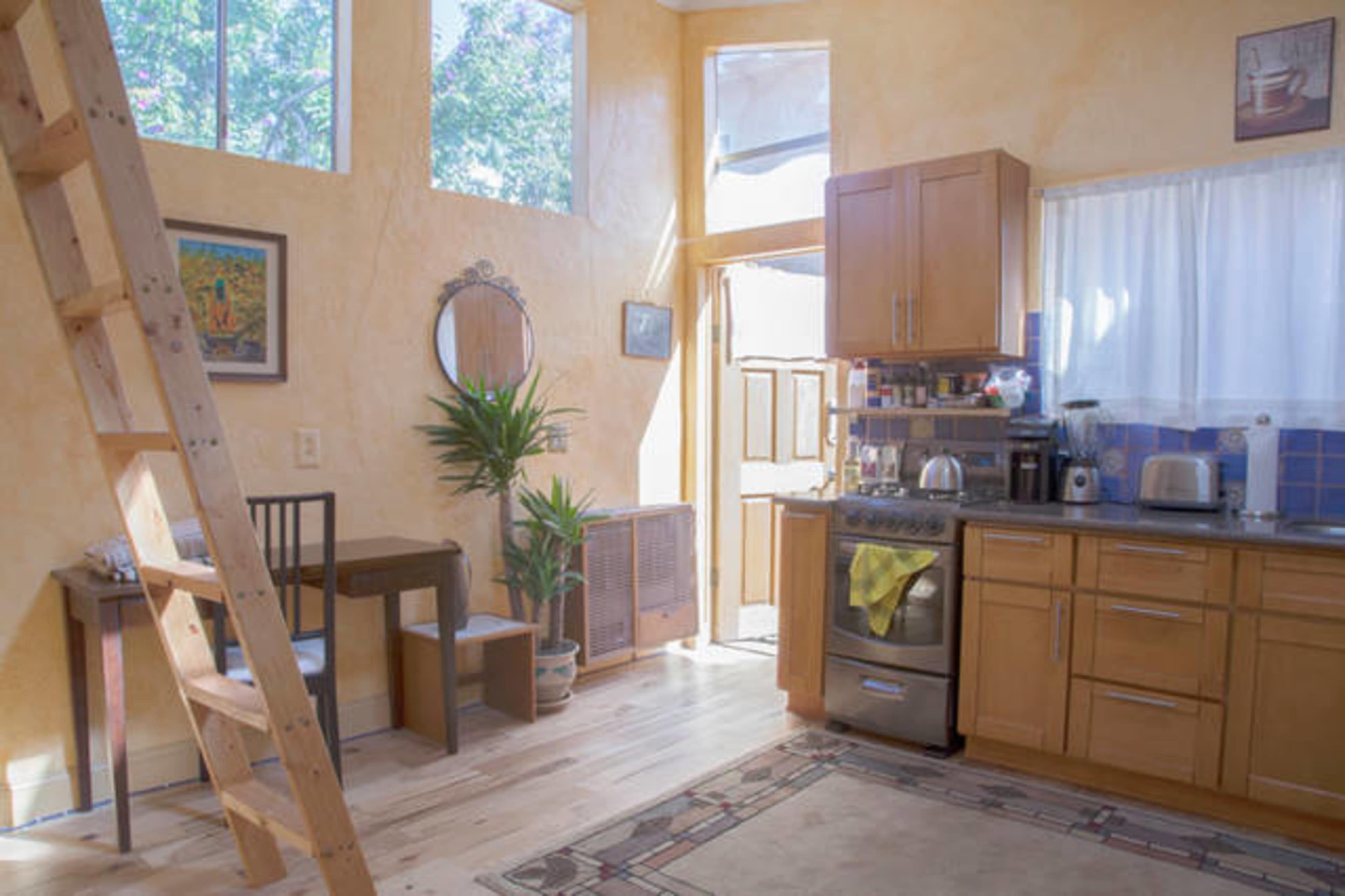 A well-lit kitchen area features wooden cabinetry, a small dining table, and a ladder leading to a loft space.
