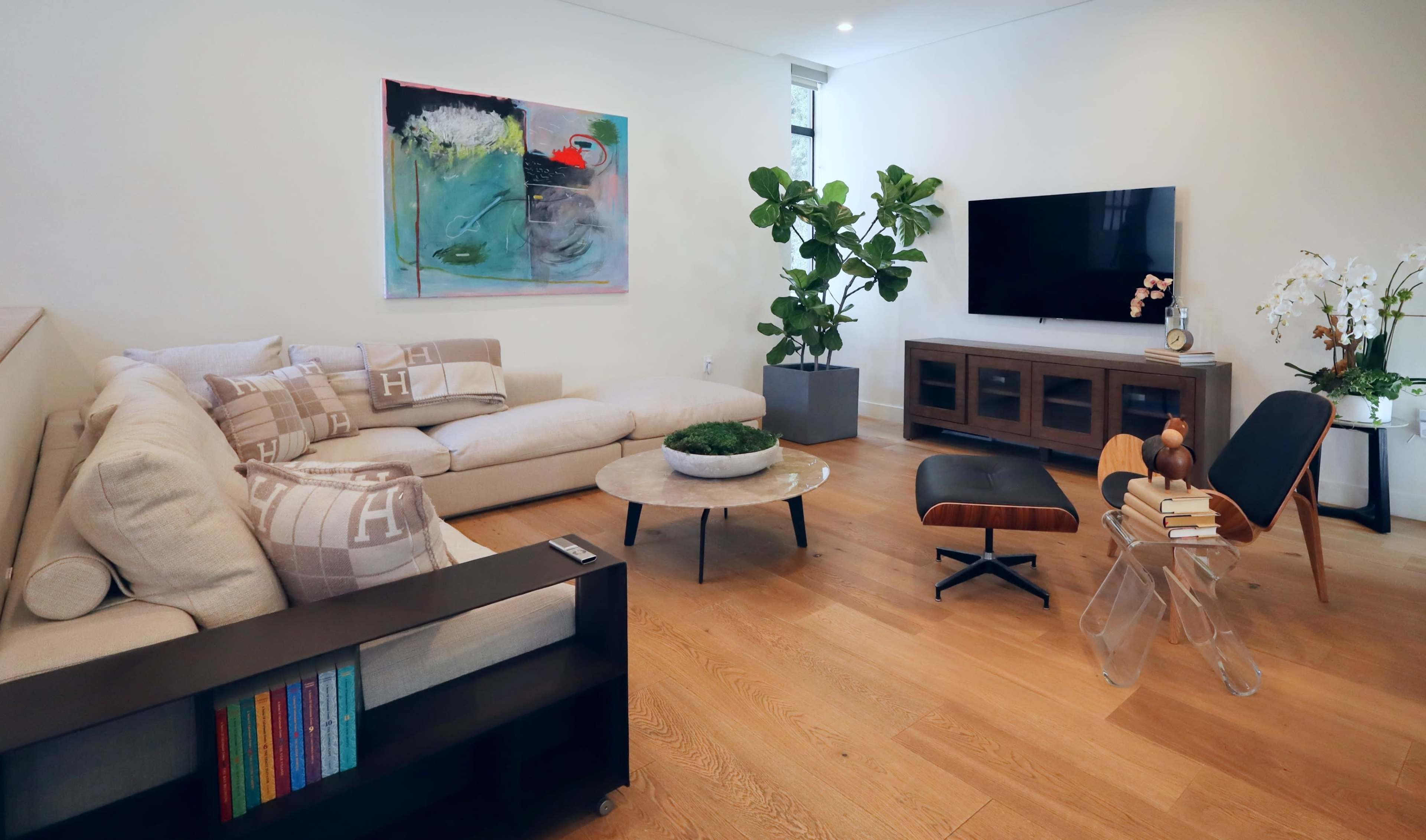 A modern living room with a sectional sofa, a round coffee table, a television mounted on the wall, and a large plant near a side table.