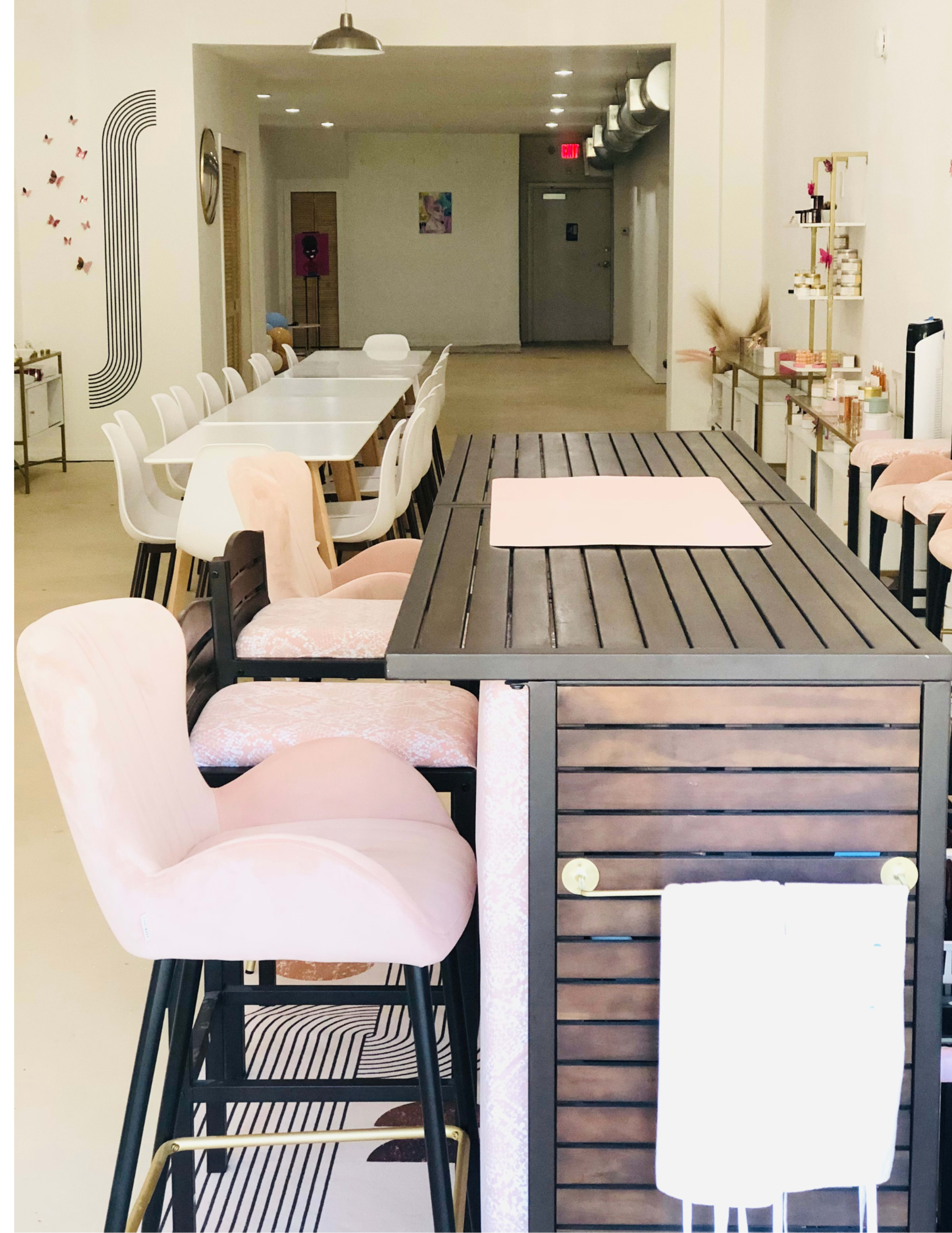 A modern, minimalist café interior with a wooden bar and pink upholstered stools, alongside tables and chairs arranged in a spacious layout.