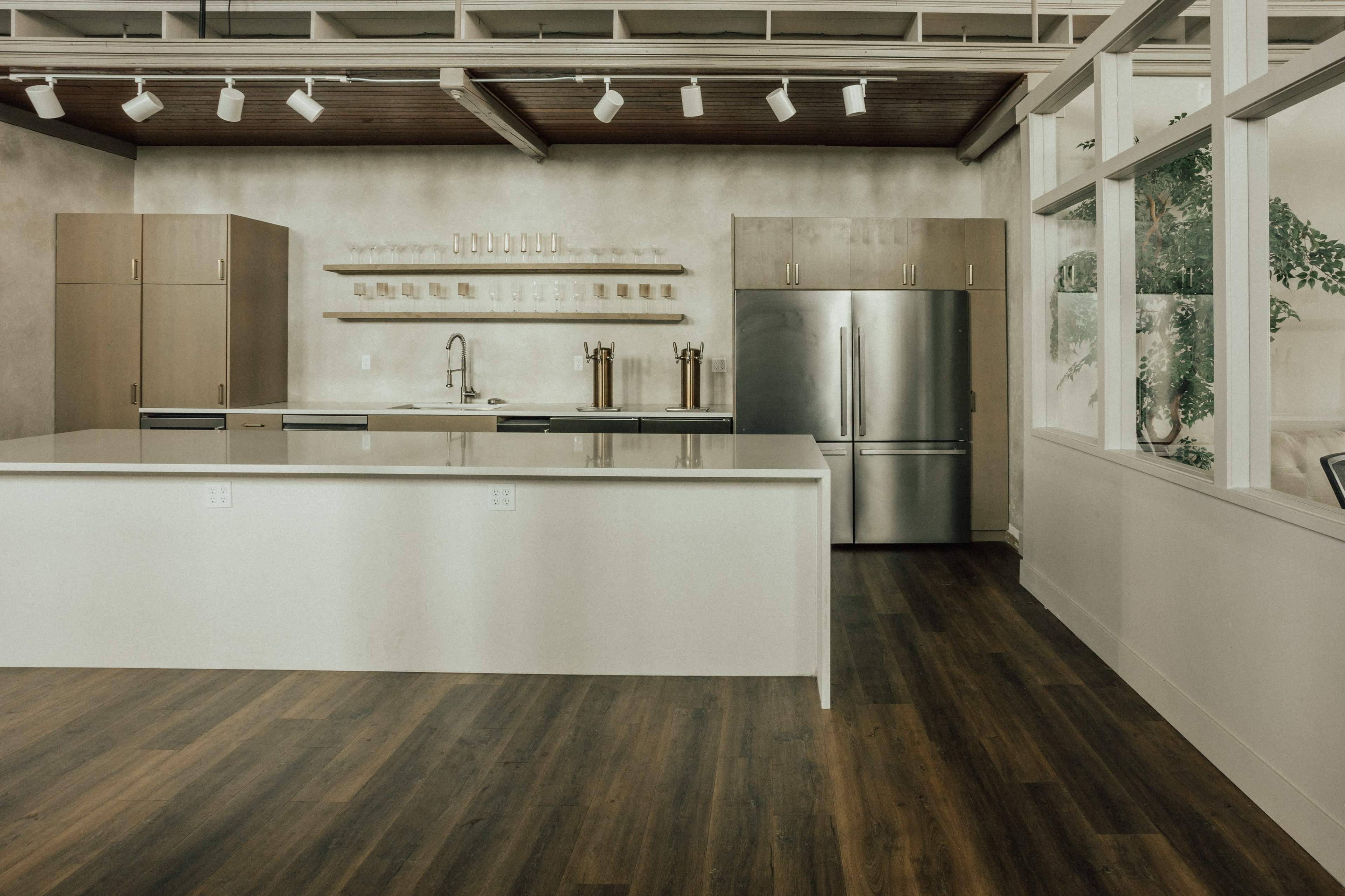 A modern kitchen with a large island, stainless steel appliances, and wooden cabinetry against a light-colored wall.