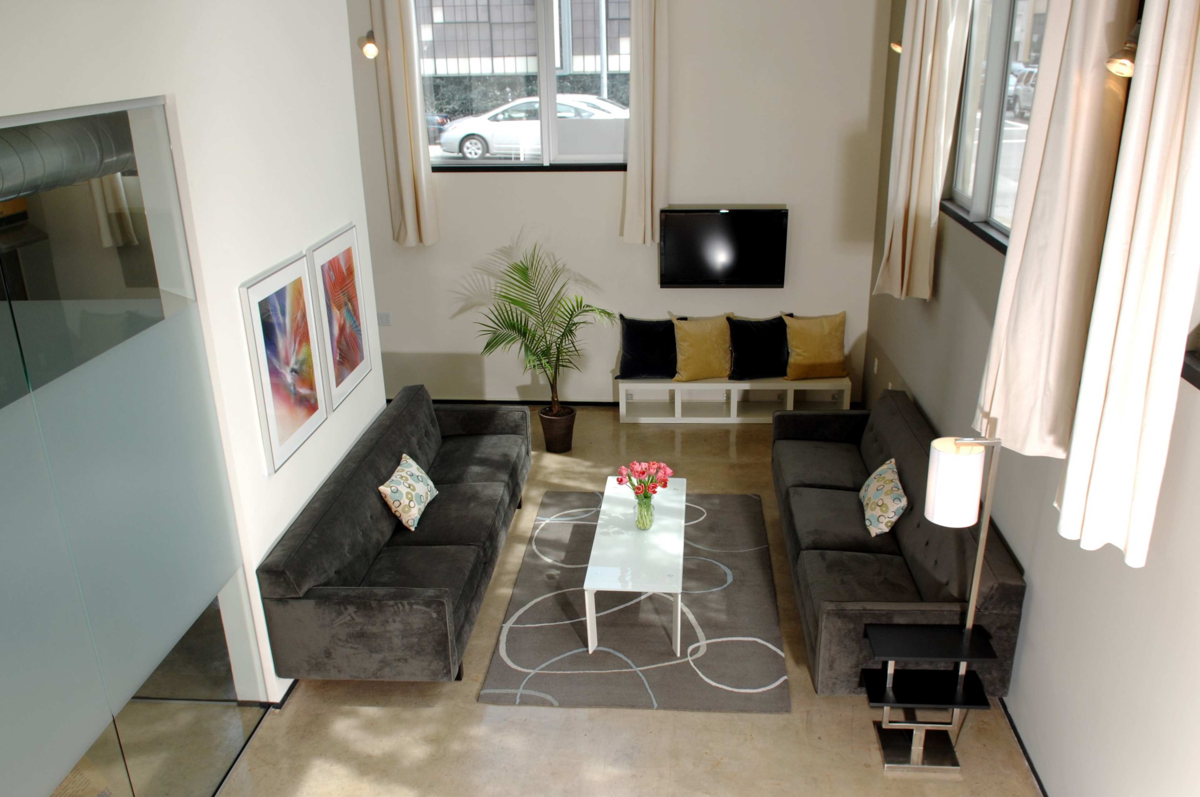 A spacious living room with two dark gray sofas, a coffee table, and decorative pillows, framed artwork on the walls, and a television mounted above a modern console.