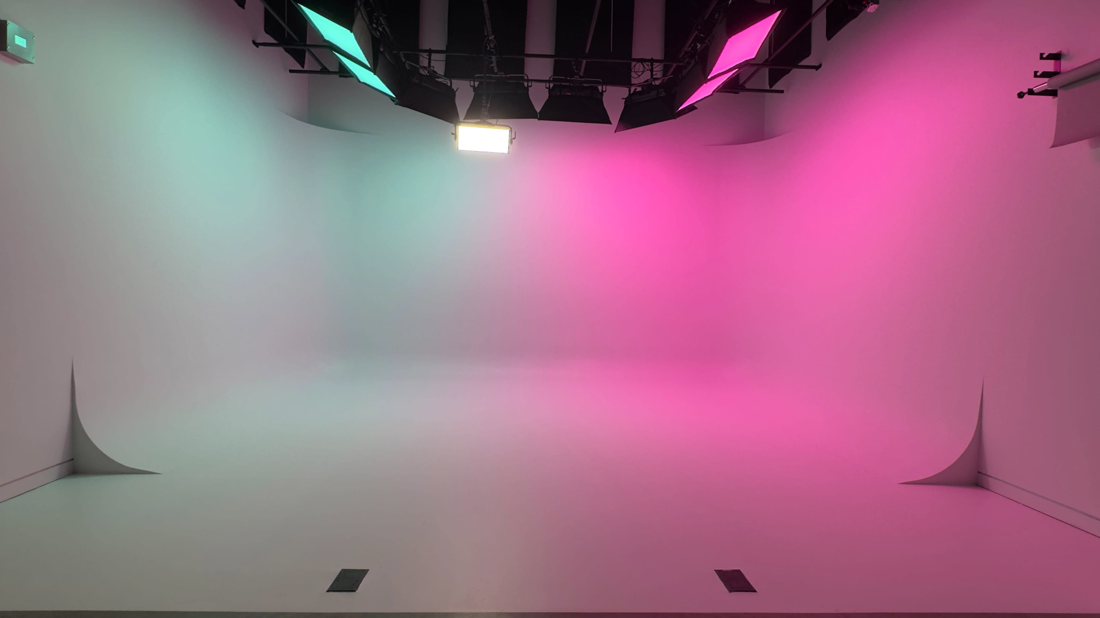 The image shows a photography studio with a blank backdrop illuminated by colorful lights in pink and green.
