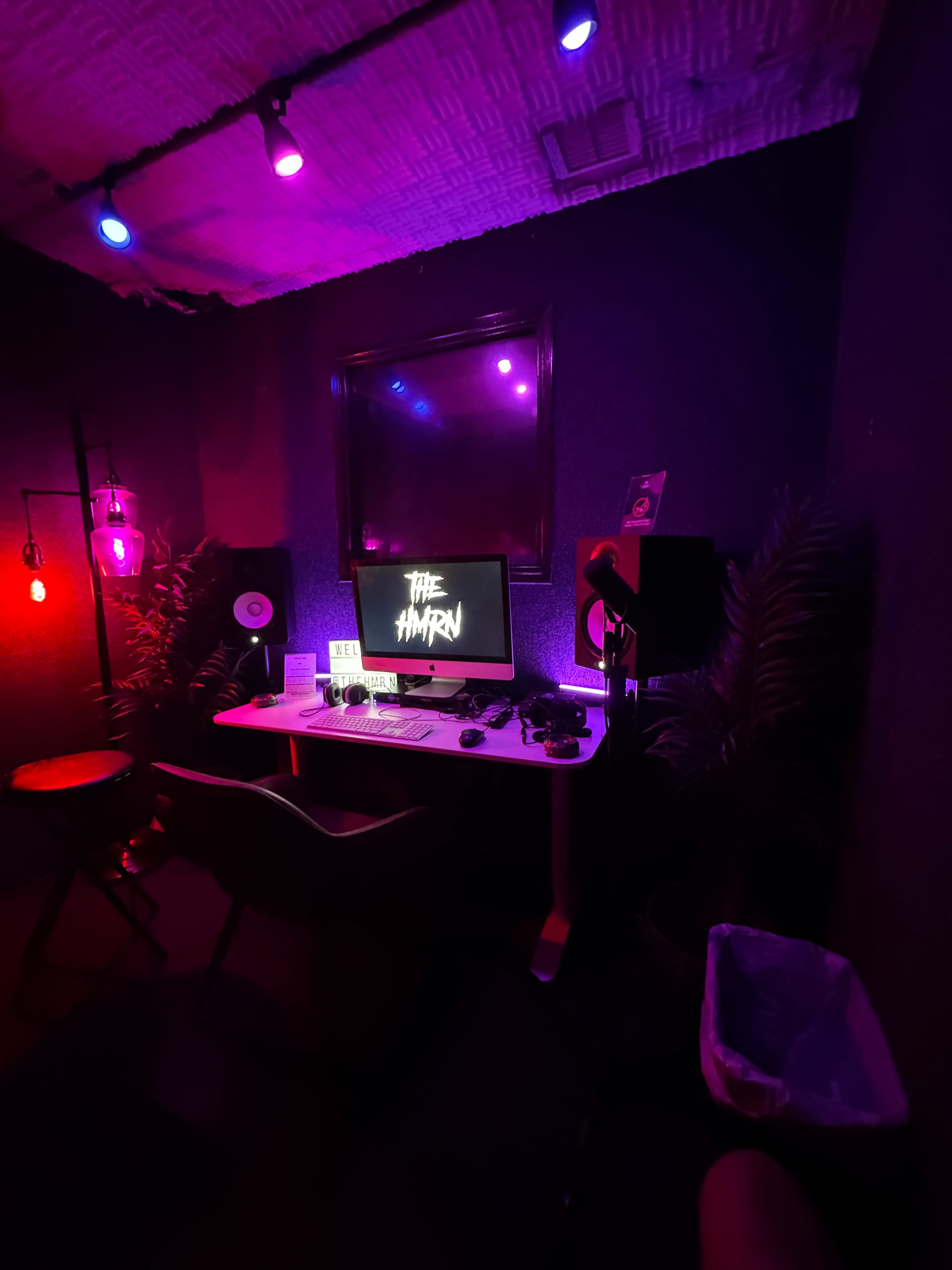 The image shows a dimly lit recording studio with a computer desk, a monitor displaying "THE HYYRN," and colorful lights illuminating the space.