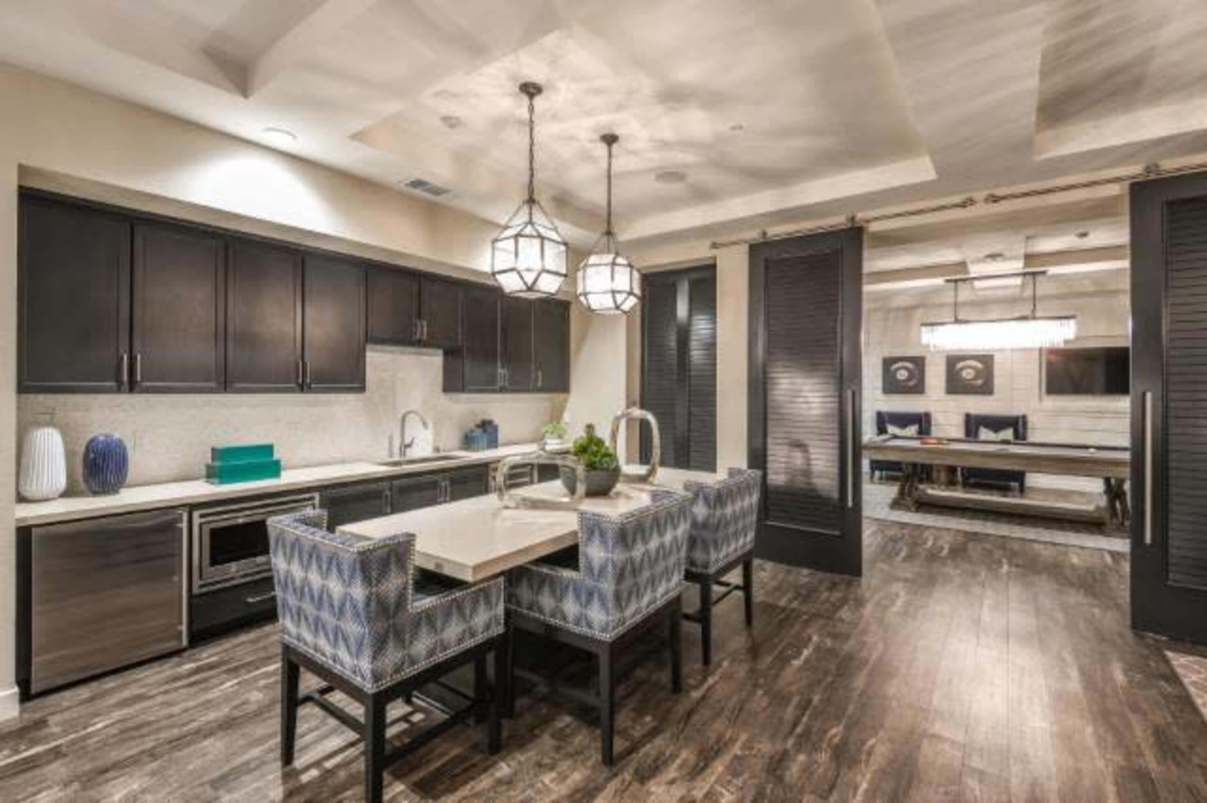 A modern kitchen and dining area with a table surrounded by patterned chairs, sleek cabinetry, and decorative pendant lights.
