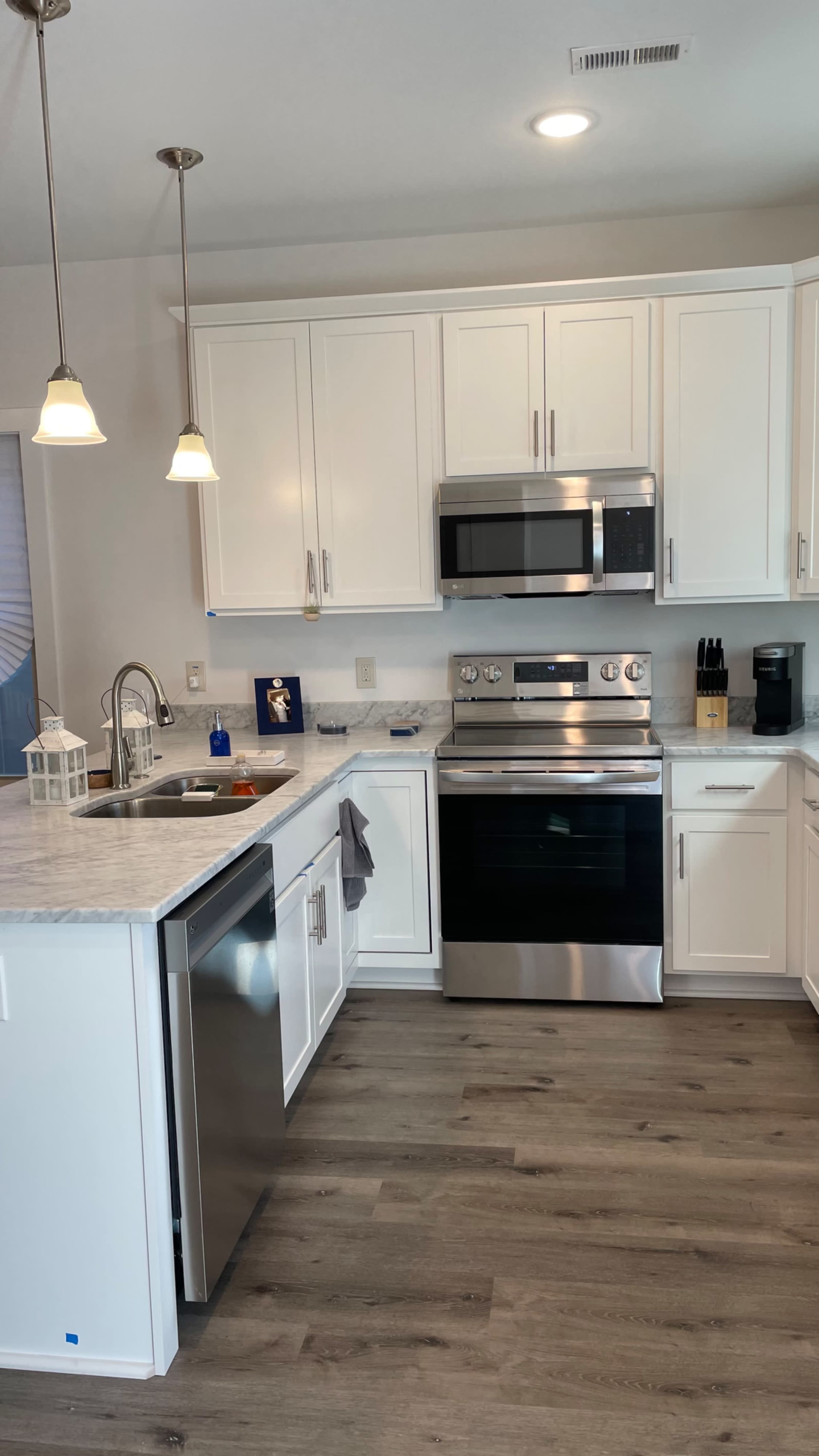 The image shows a modern kitchen featuring white cabinets, stainless steel appliances, and a marble countertop.