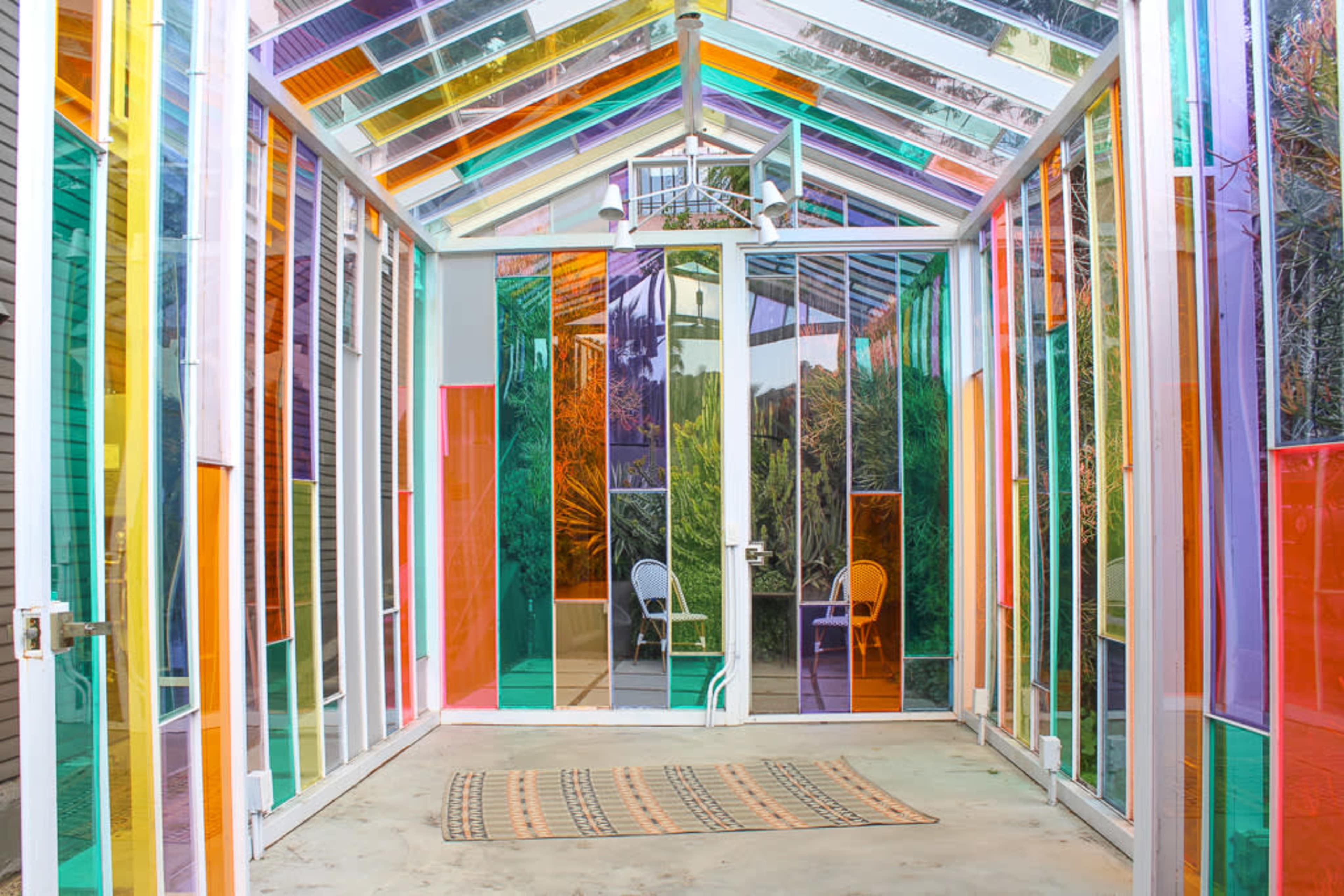 The image shows a colorful glass room filled with transparent panels creating a spectrum of light and reflections.