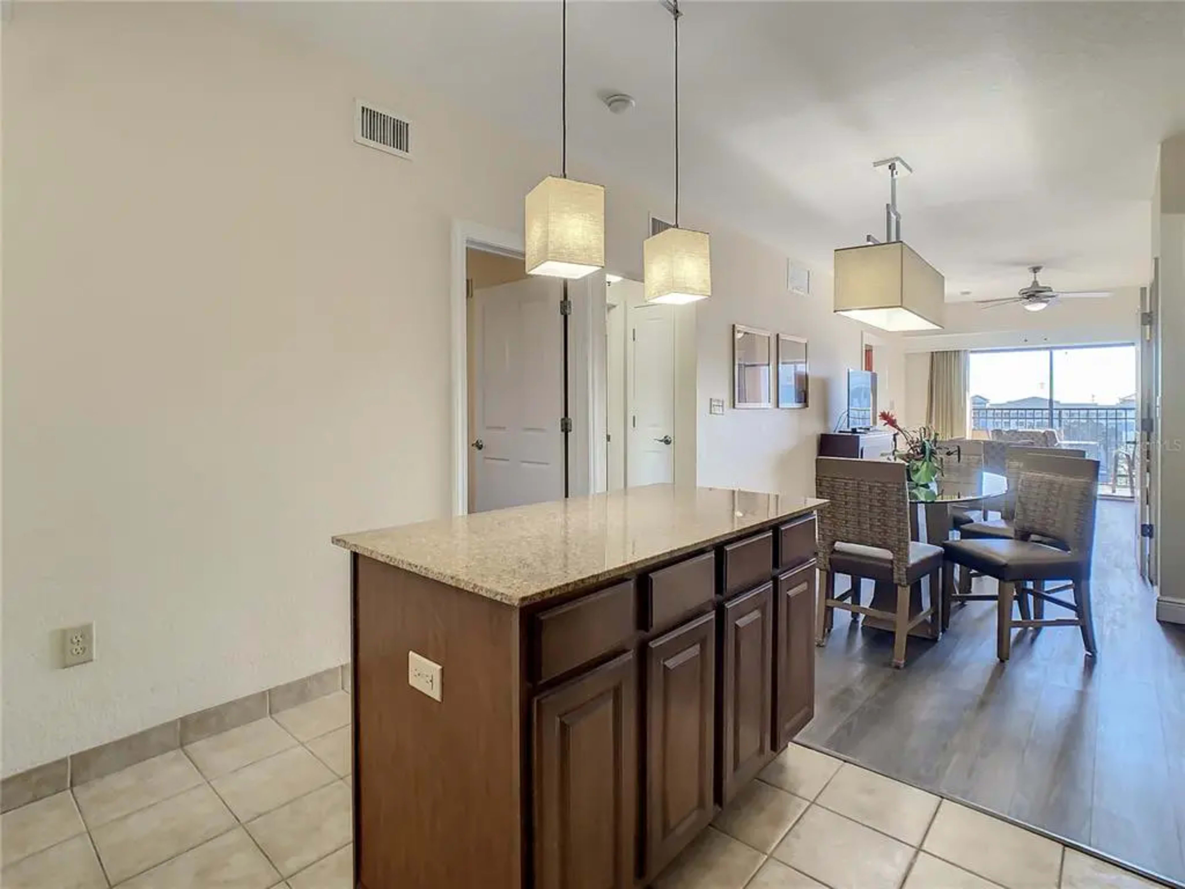 A modern kitchen area featuring a granite-topped island, pendant lighting, and a dining table with chairs.