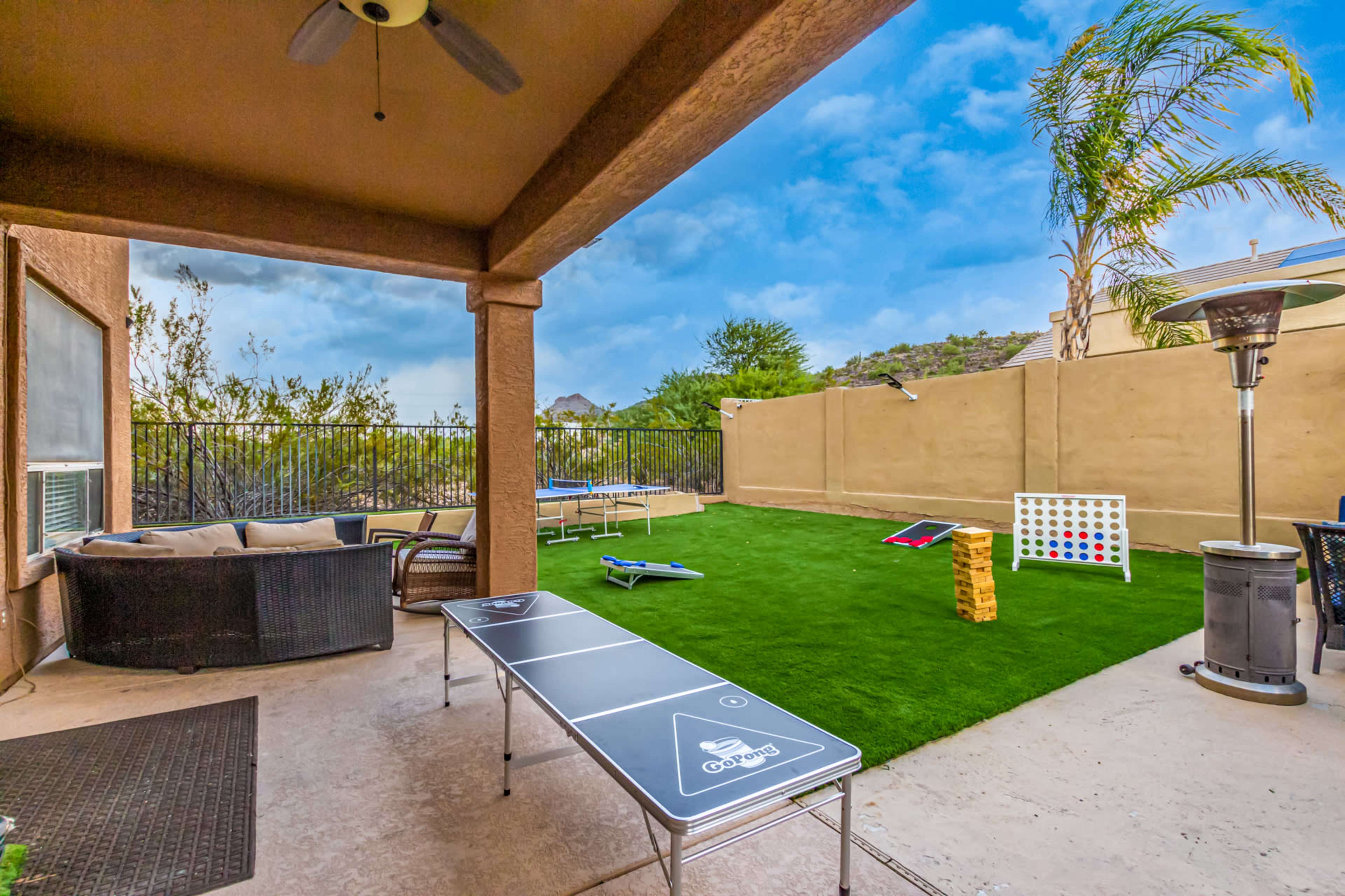 The image shows a patio area with a grass lawn, a table for games, lounge seating, and various outdoor game setups.