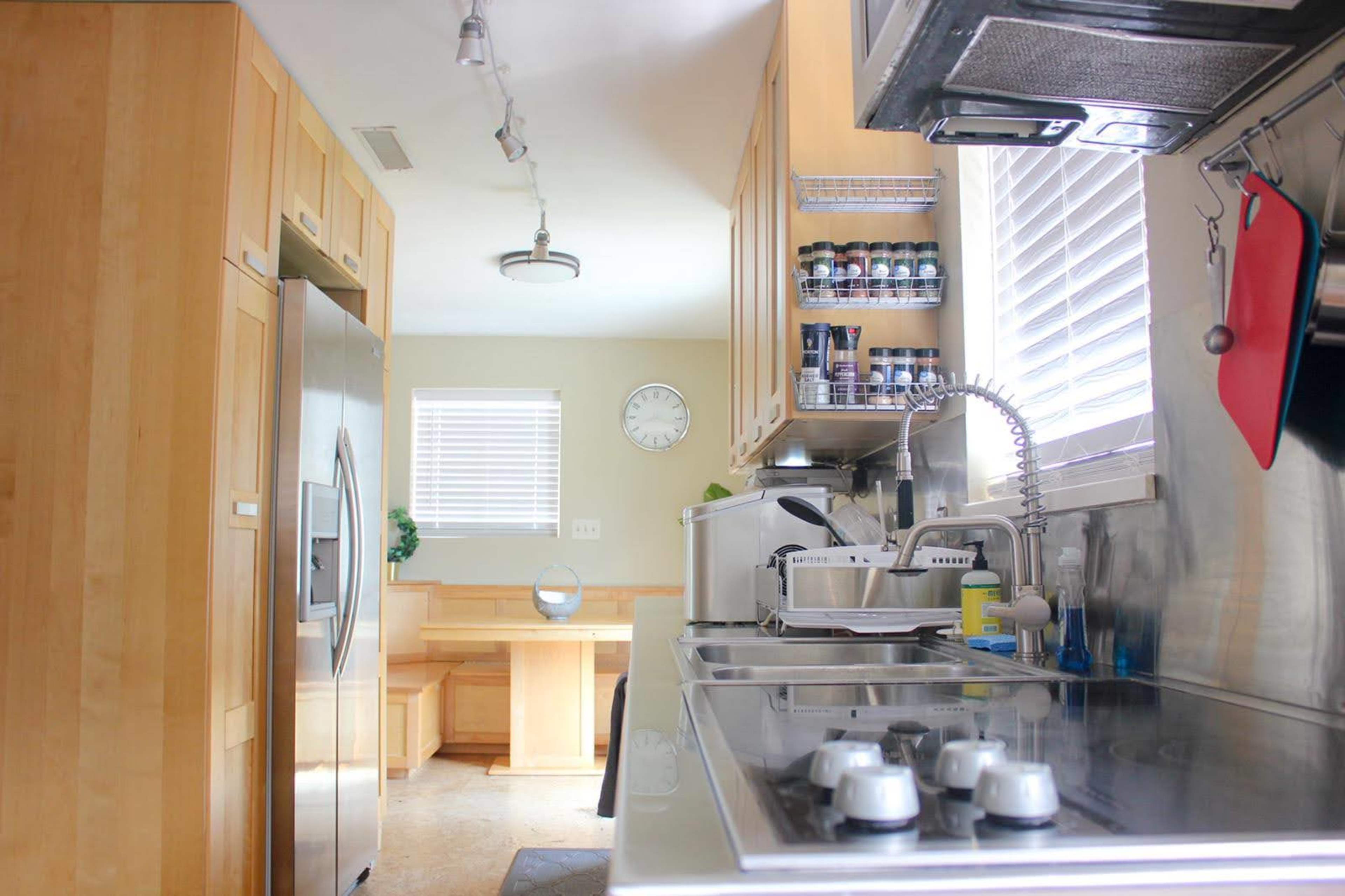 A modern kitchen features stainless steel appliances, wooden cabinetry, and a small dining area with a clock on the wall.