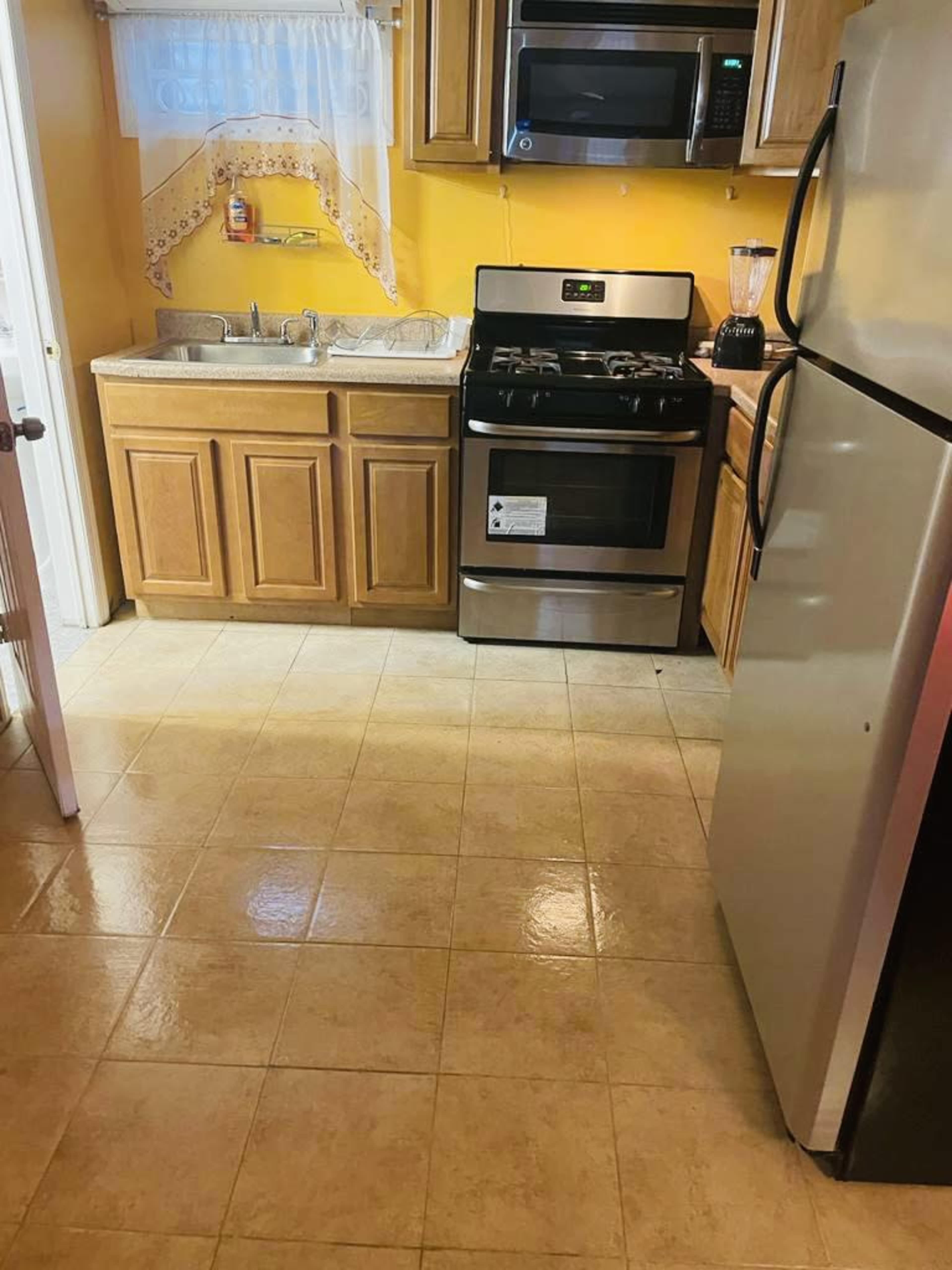 A kitchen with a yellow wall, stainless steel appliances, a sink, and wooden cabinets.