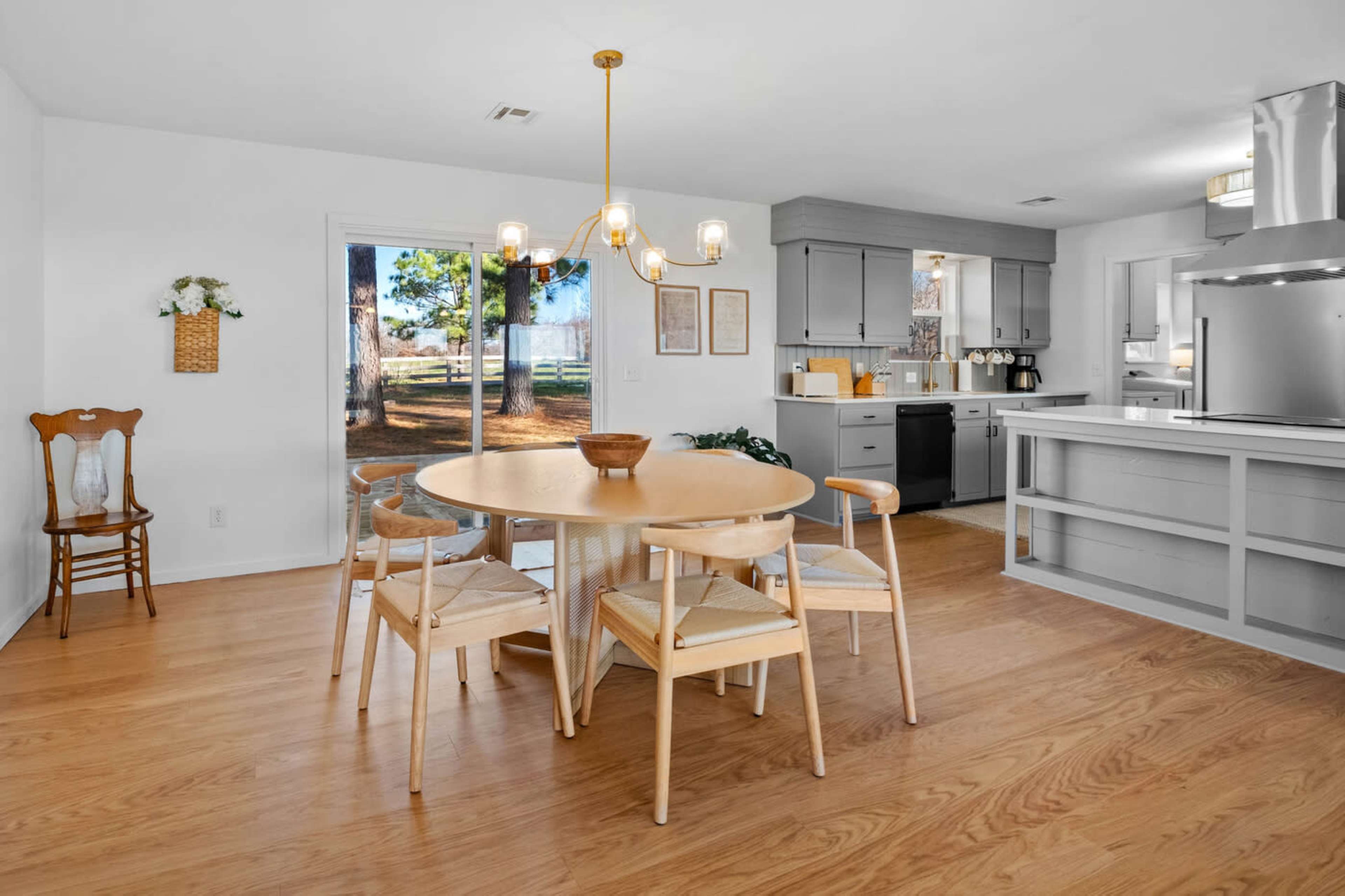 A dining area features a round table surrounded by wooden chairs, with a view of the outdoors through sliding glass doors.