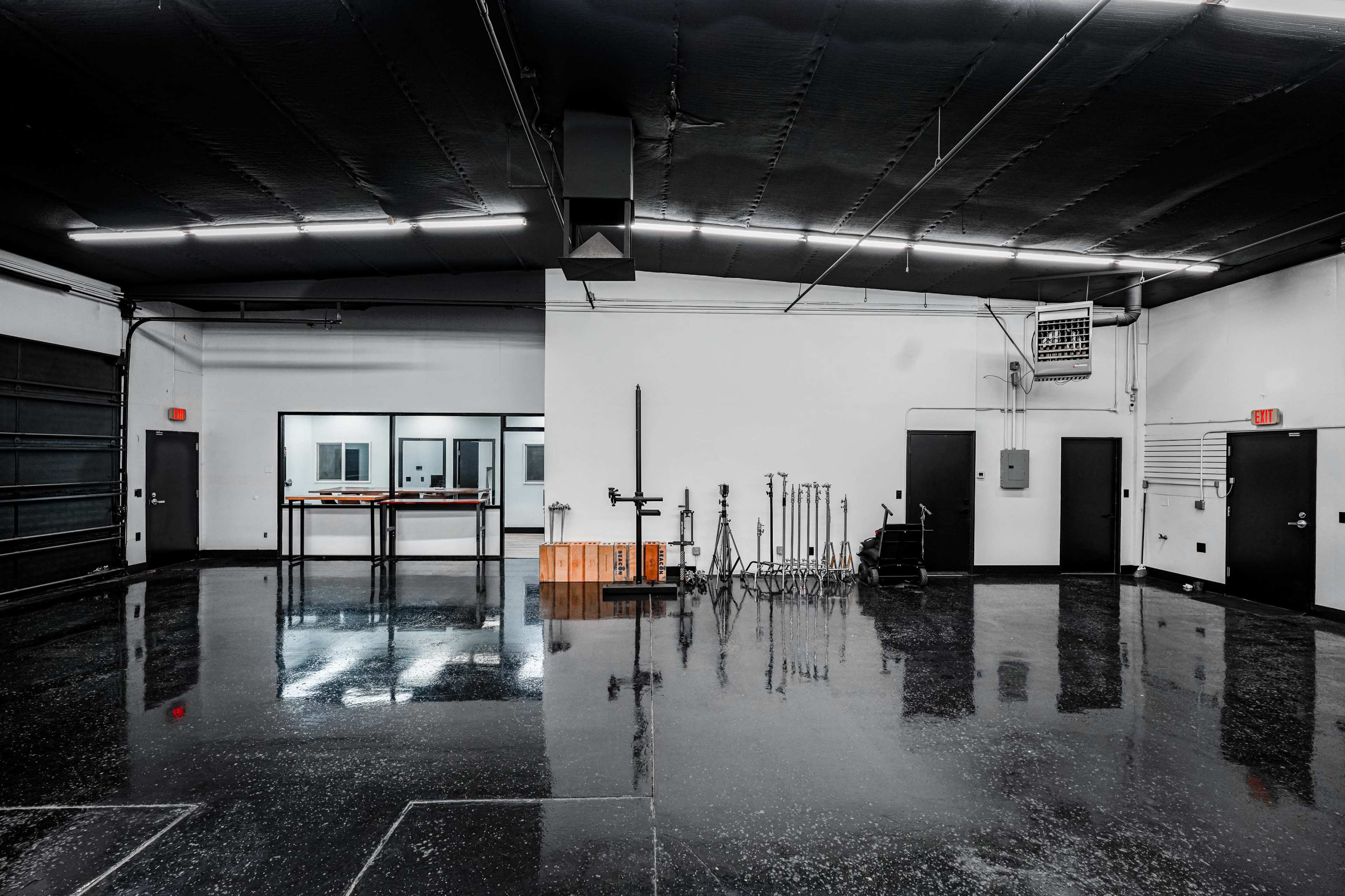 The image shows a spacious, industrial-style room with polished black floors, large windows, and various equipment stands arranged along one wall.