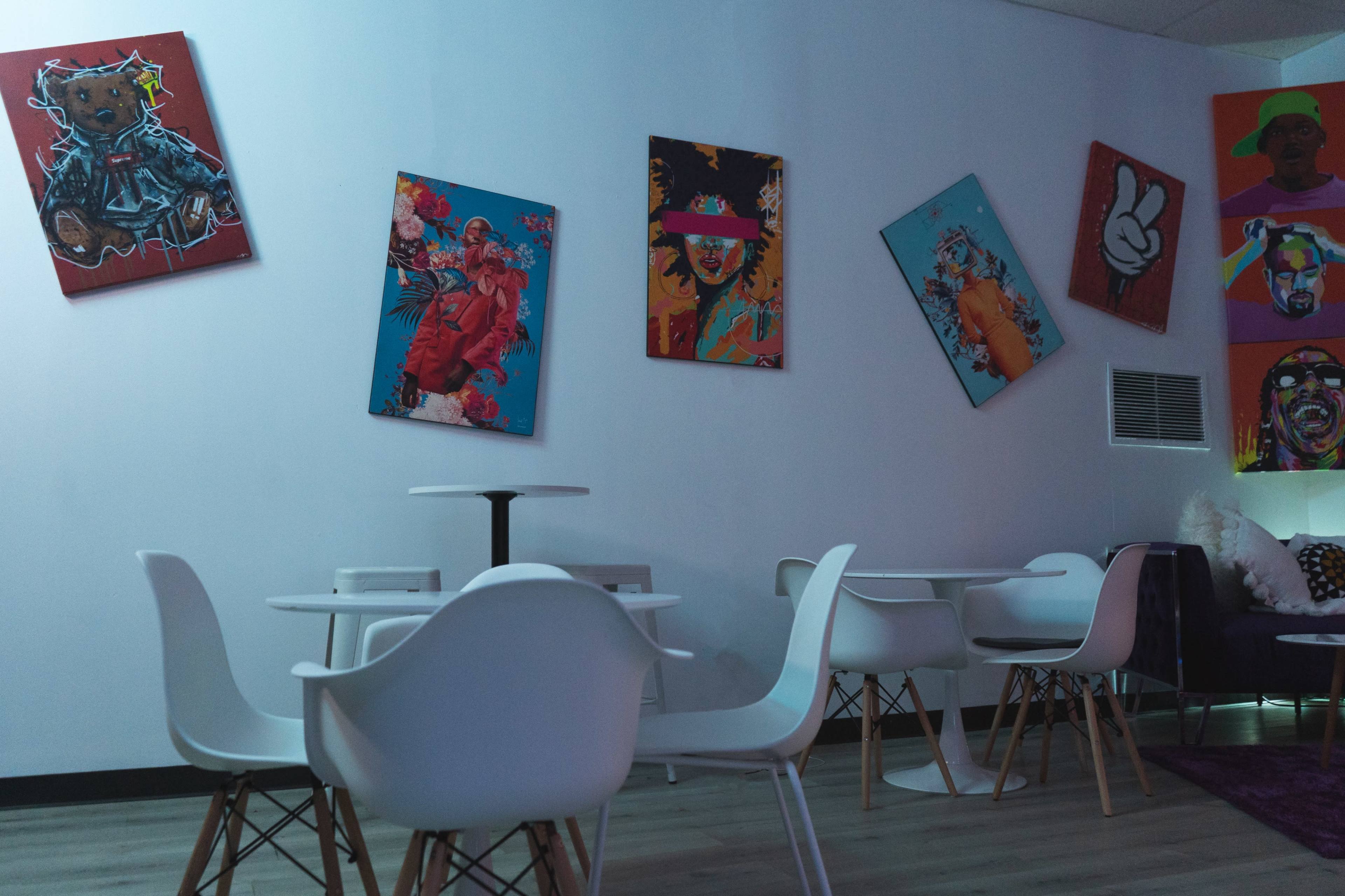 A modern indoor space featuring white chairs and tables arranged around a wall decorated with colorful artwork.