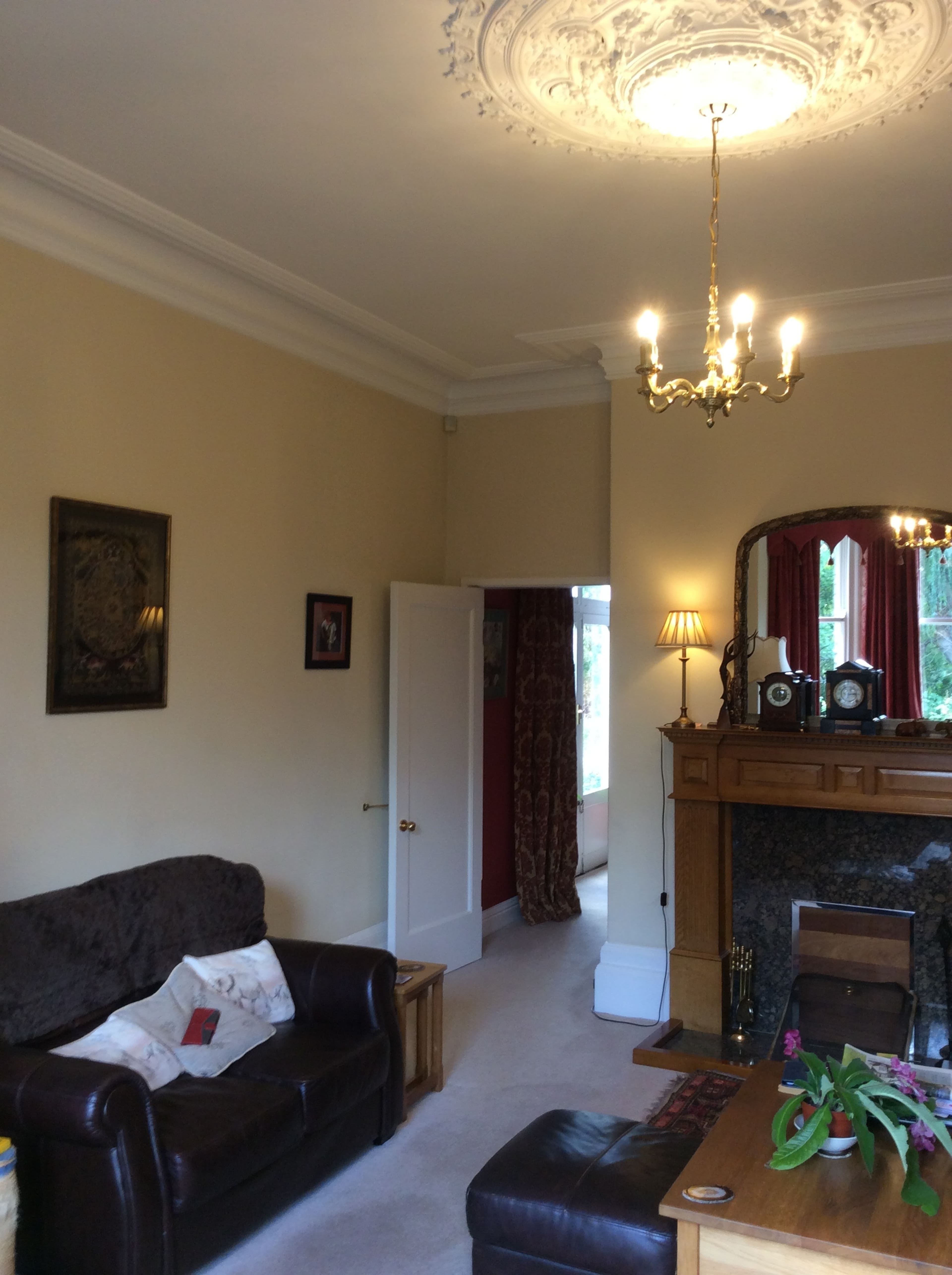 A living room with a brown leather sofa, a wooden table, and a decorative fireplace under an ornate ceiling light.