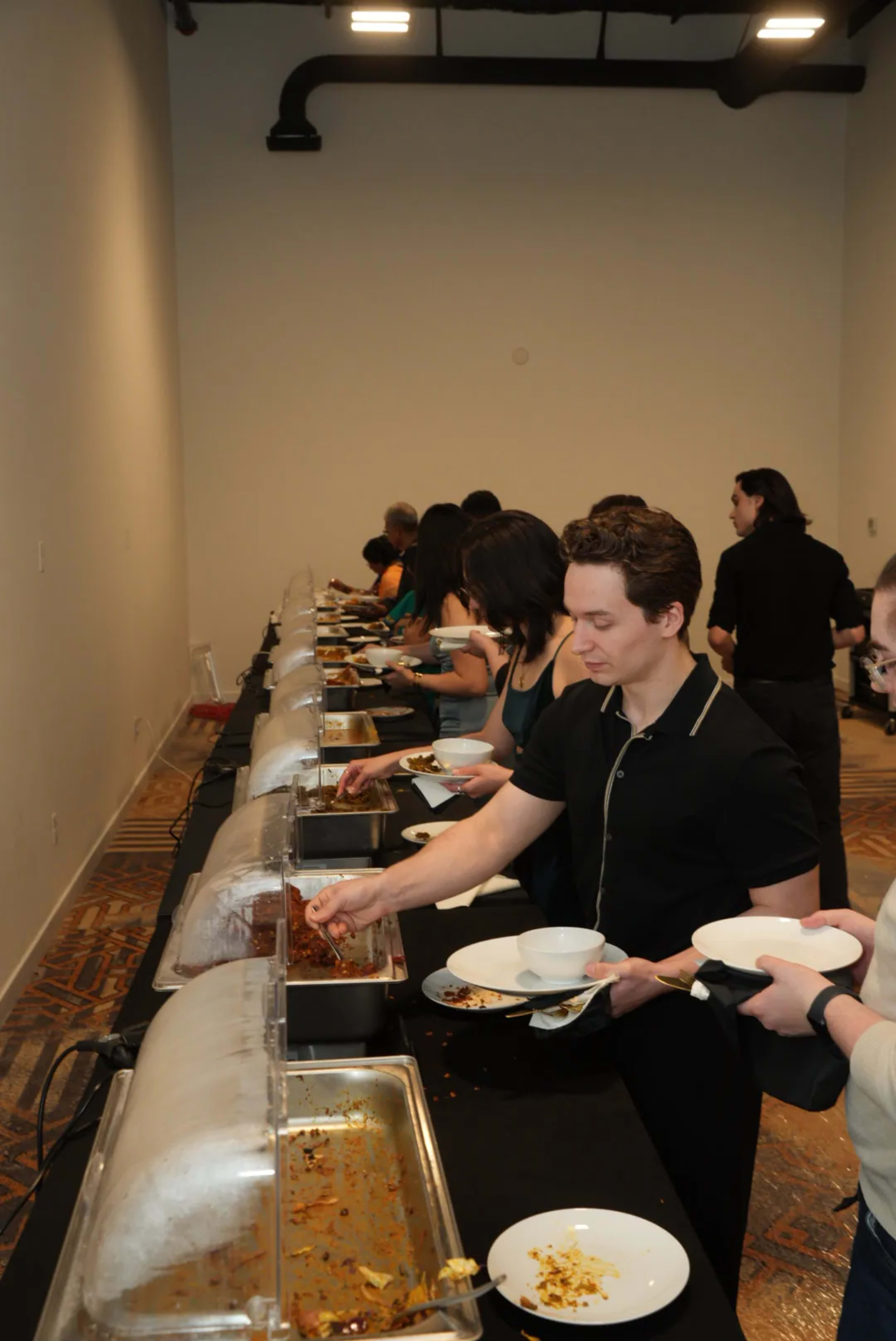 A group of people are serving themselves food from a buffet table in a conference room.