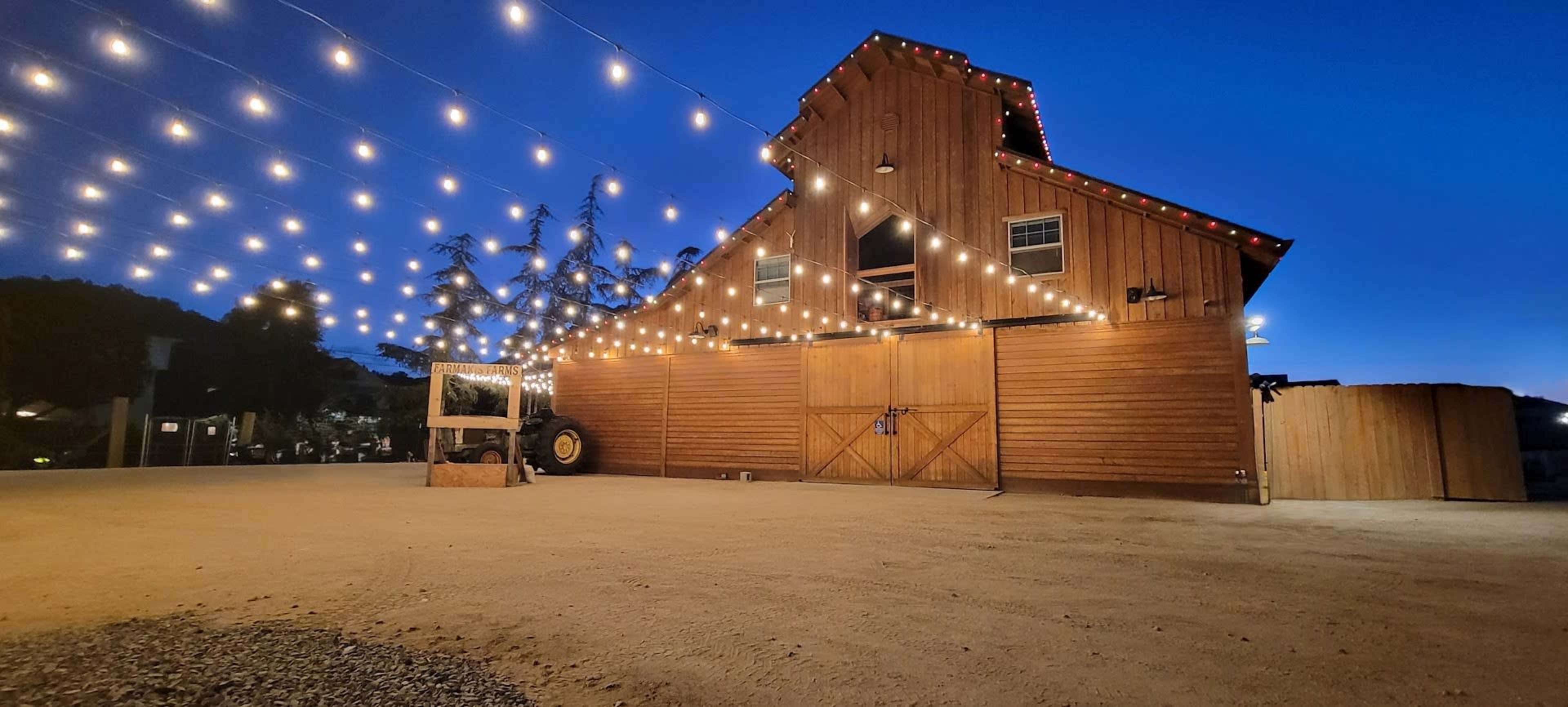 A wooden barn is illuminated by string lights against a twilight sky.