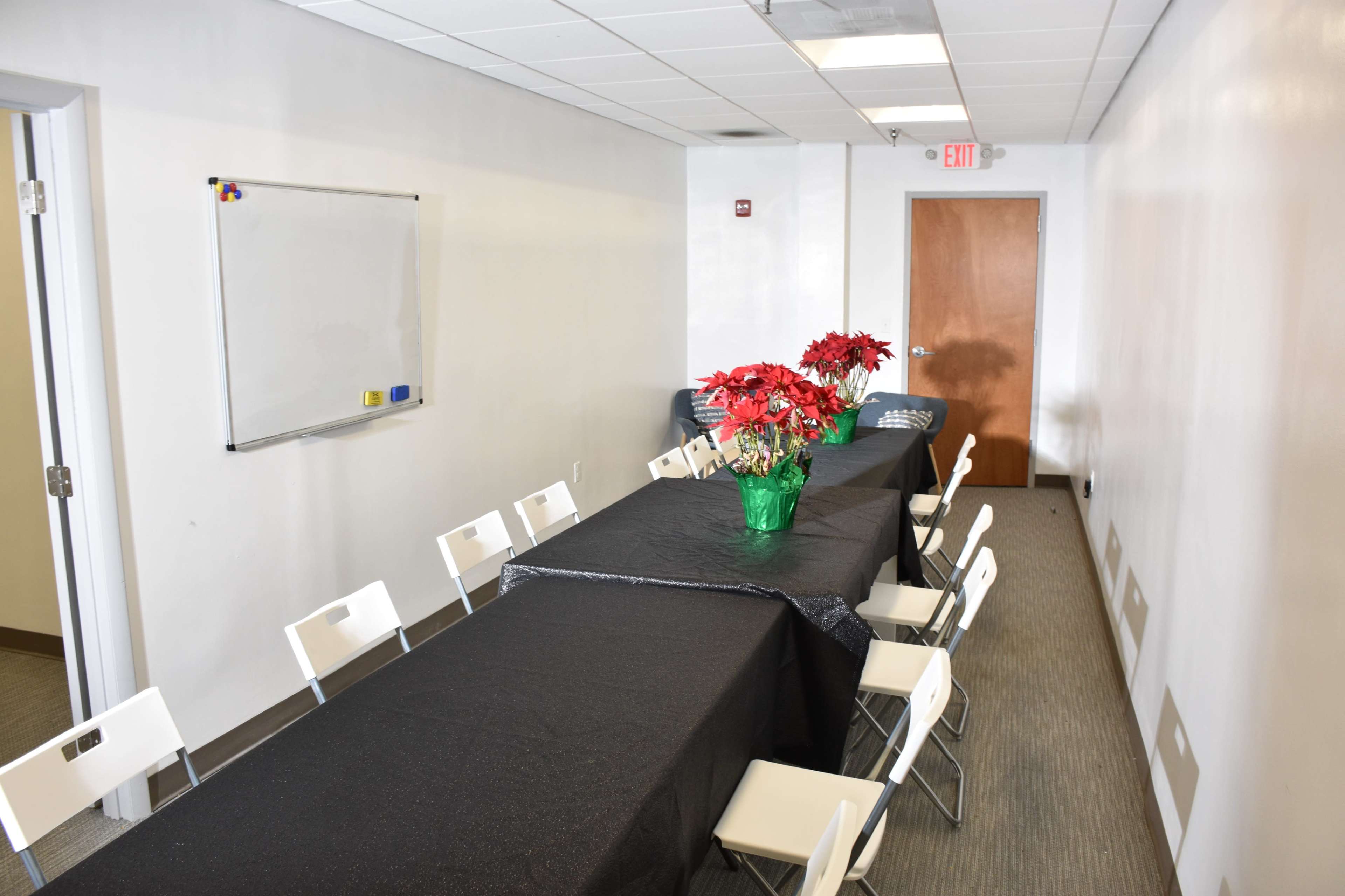 A long table covered in a black tablecloth is set up in a brightly lit meeting room with white walls and chairs on either side.