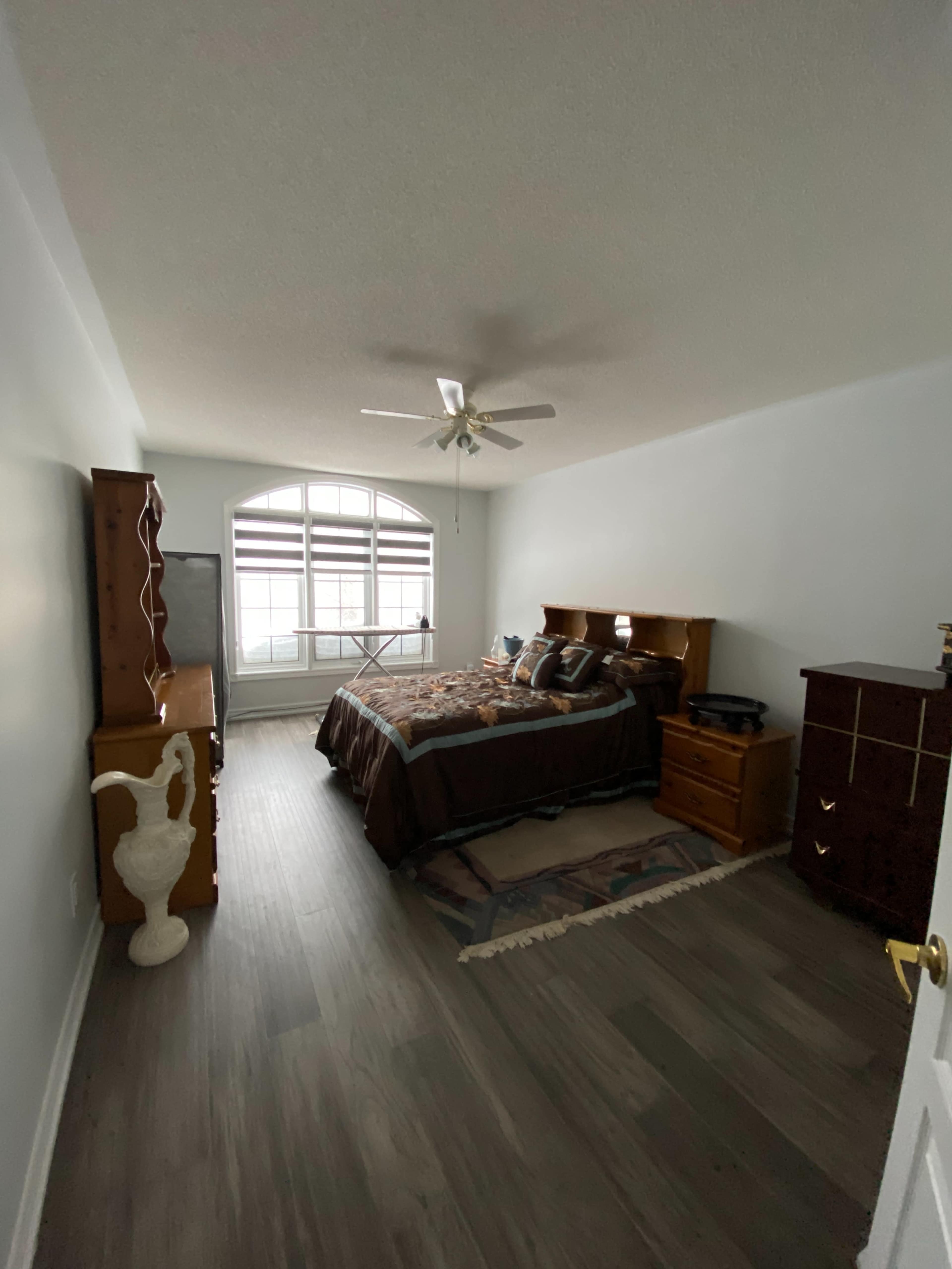 A bedroom with a bed, nightstands, a decorative dresser, and a large window allowing natural light to enter.