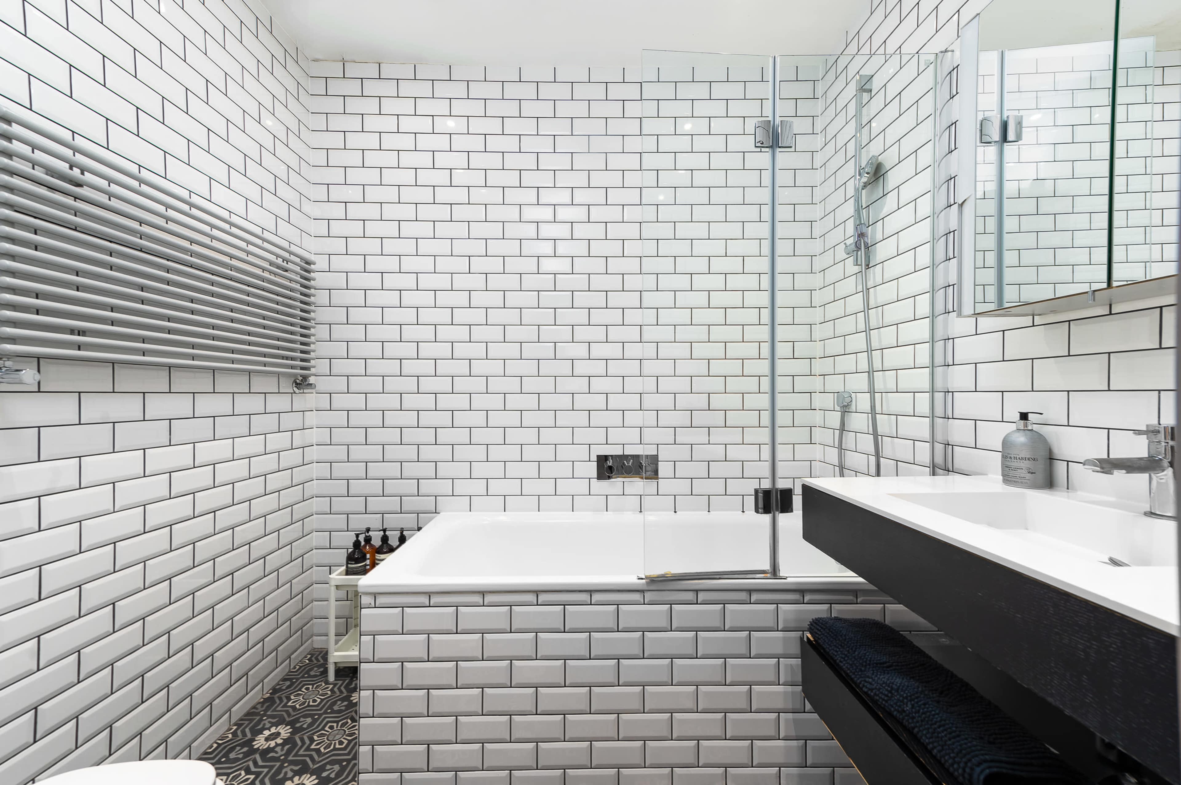 The bathroom features white subway tile on the walls and a patterned floor, with a bathtub, a shower, and a double sink vanity.