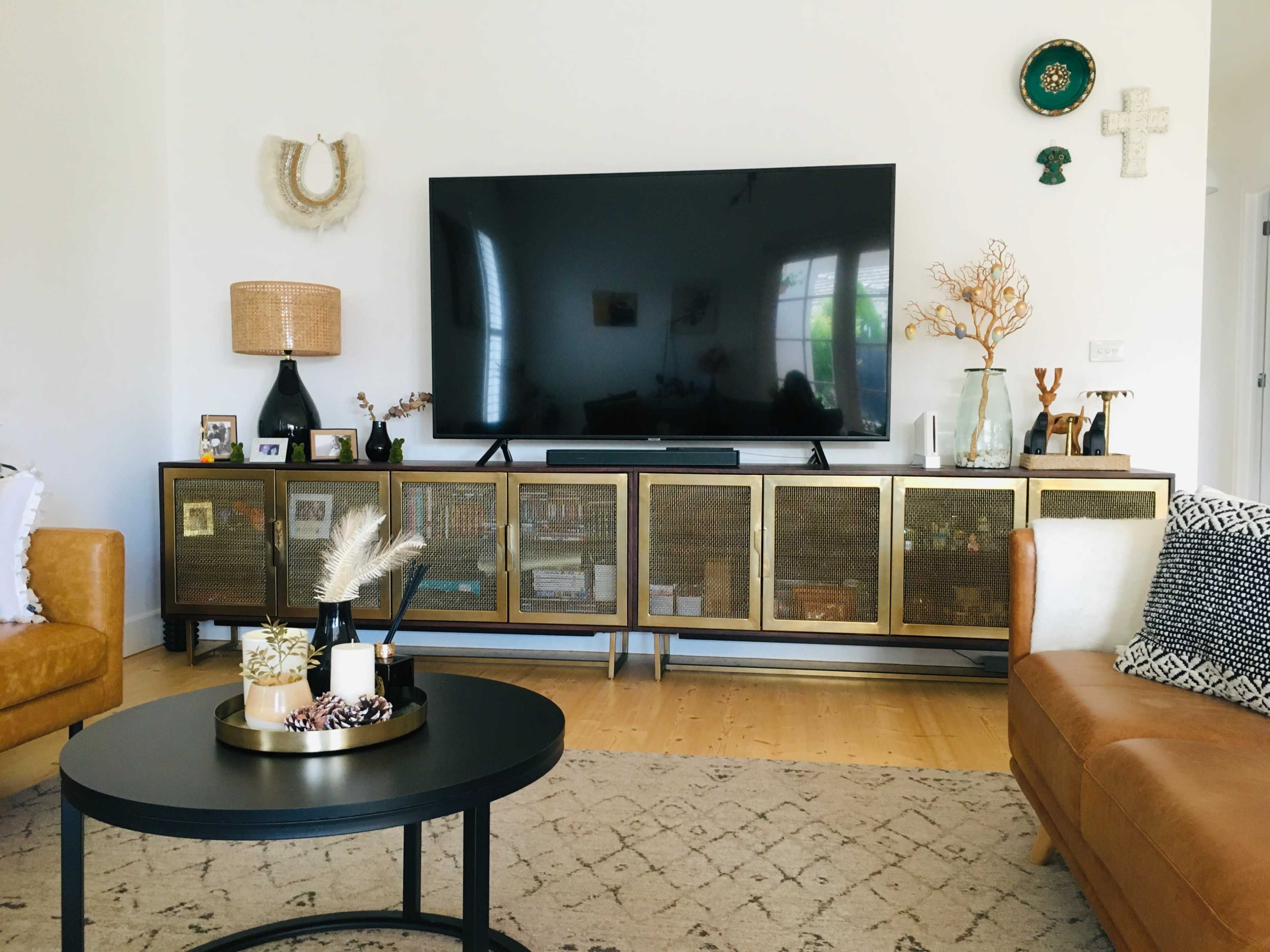 A modern living room featuring a large television mounted on the wall above a stylish media console with glass-paneled doors, surrounded by decorative items and plants.