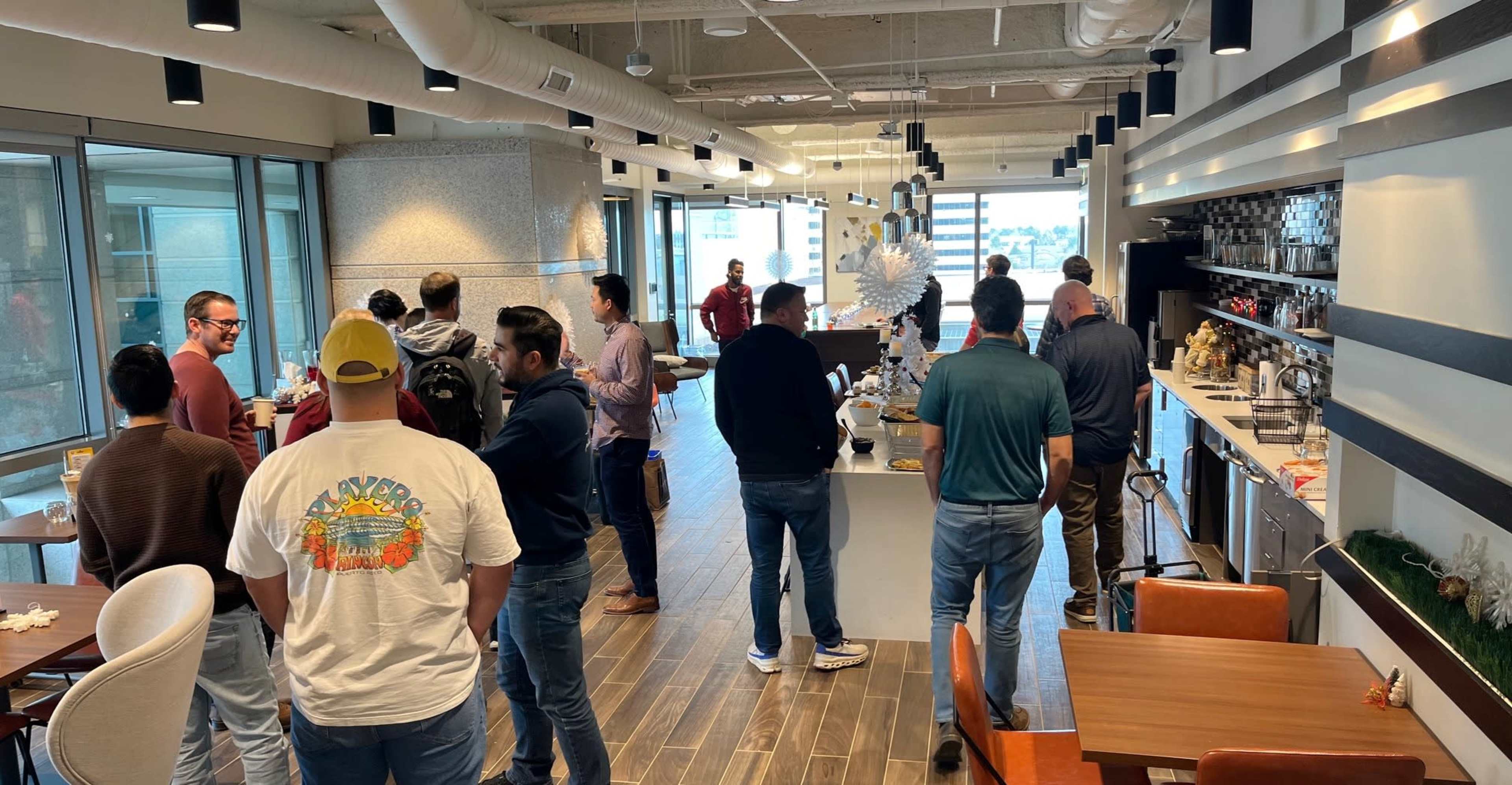 A group of people stands in a modern kitchen area, engaging in conversation while food and drinks are displayed on the counter.