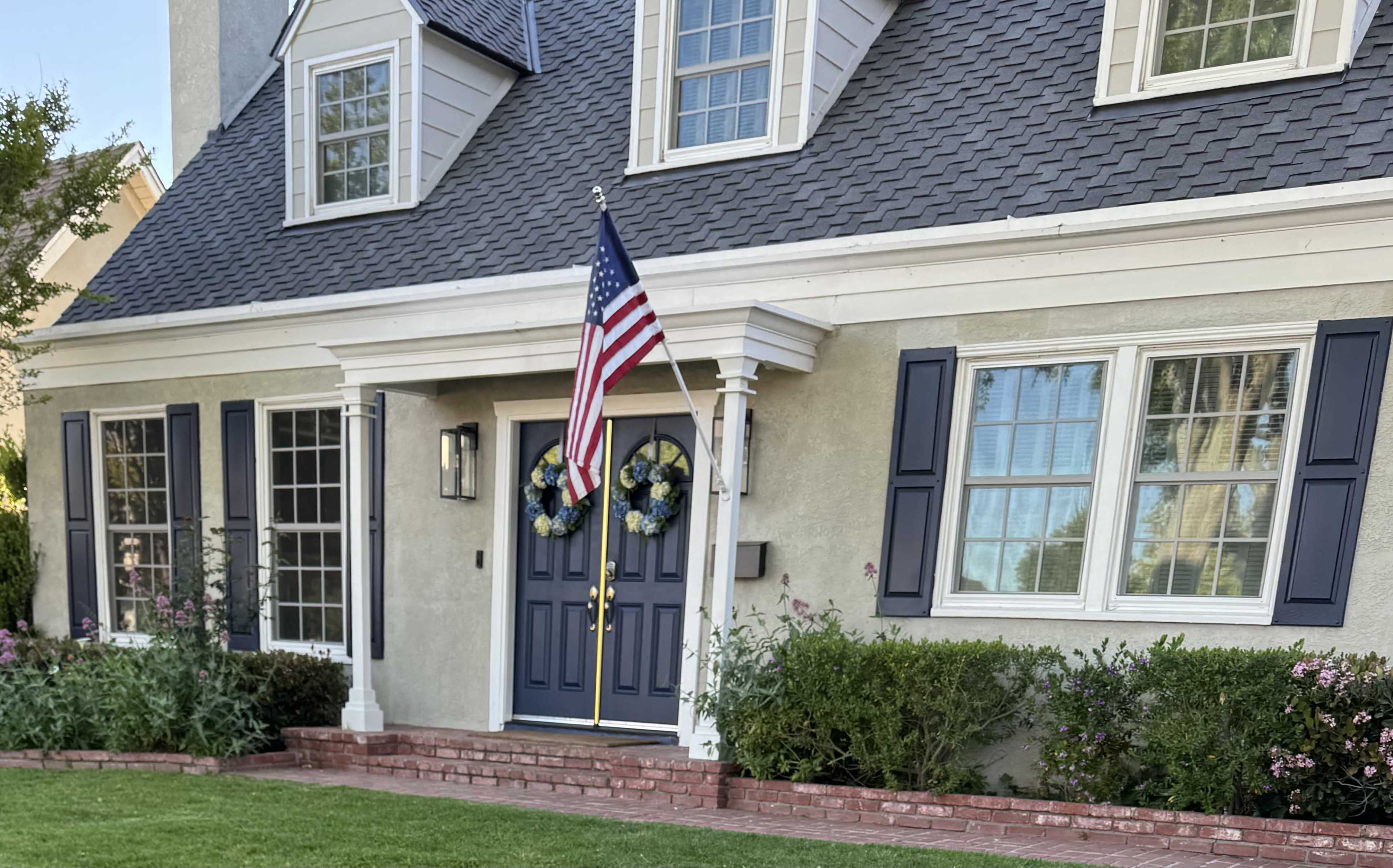A house features a blue door with an American flag hanging from the porch and decorative wreaths on either side.